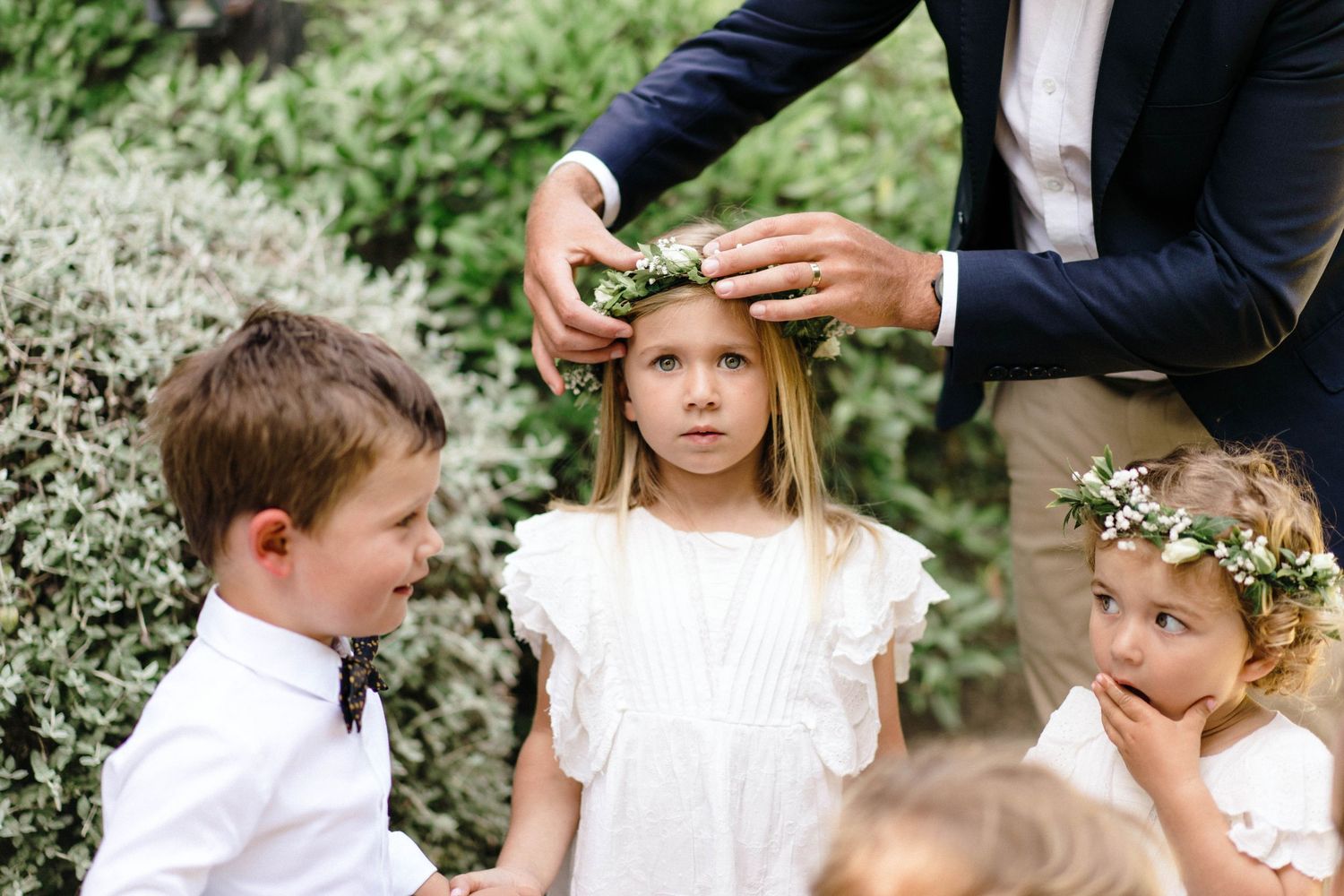 Wedding party members wearing navy suits and white dresses pose in a garden setting.