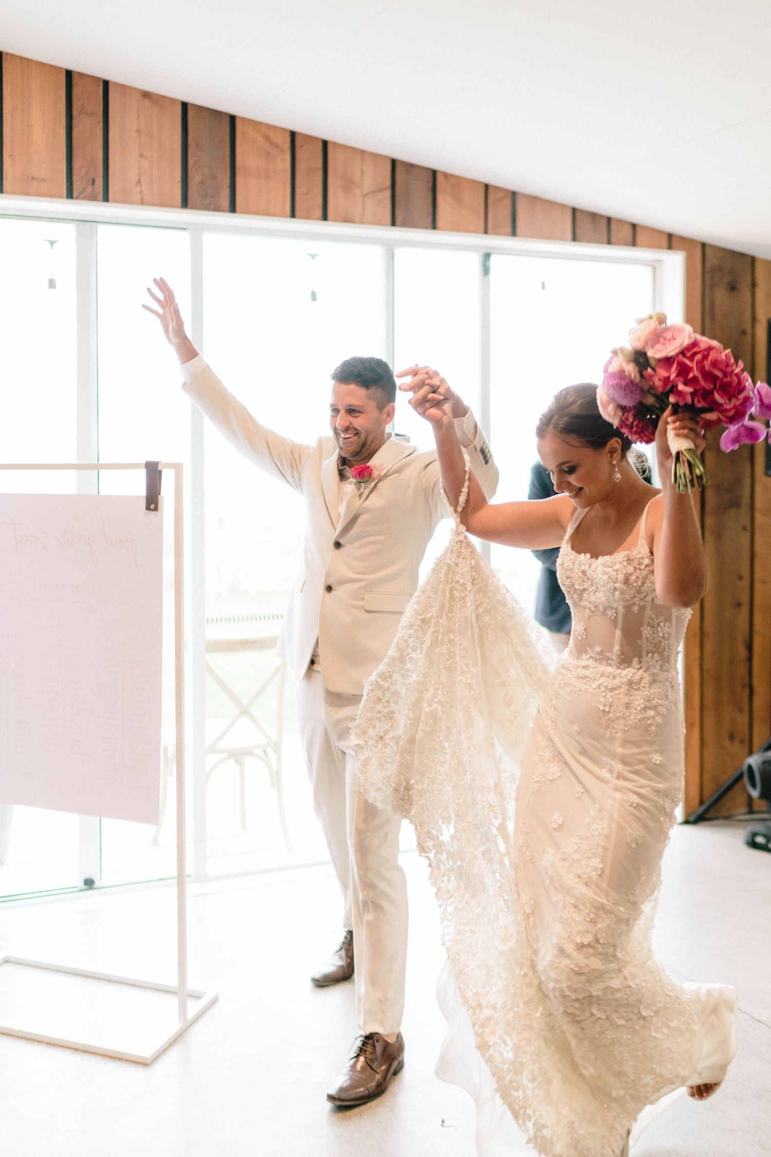 A couple dances joyfully in a bright room with wooden paneled walls and large windows.