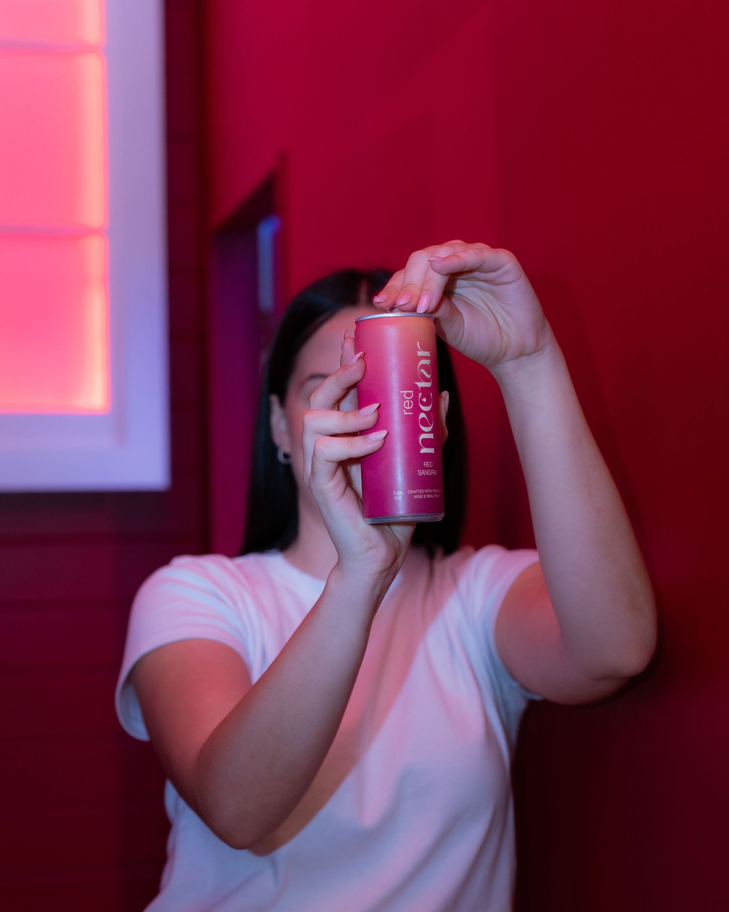 Person in dramatic red lighting holding up a pink and black cylindrical object covering their face.