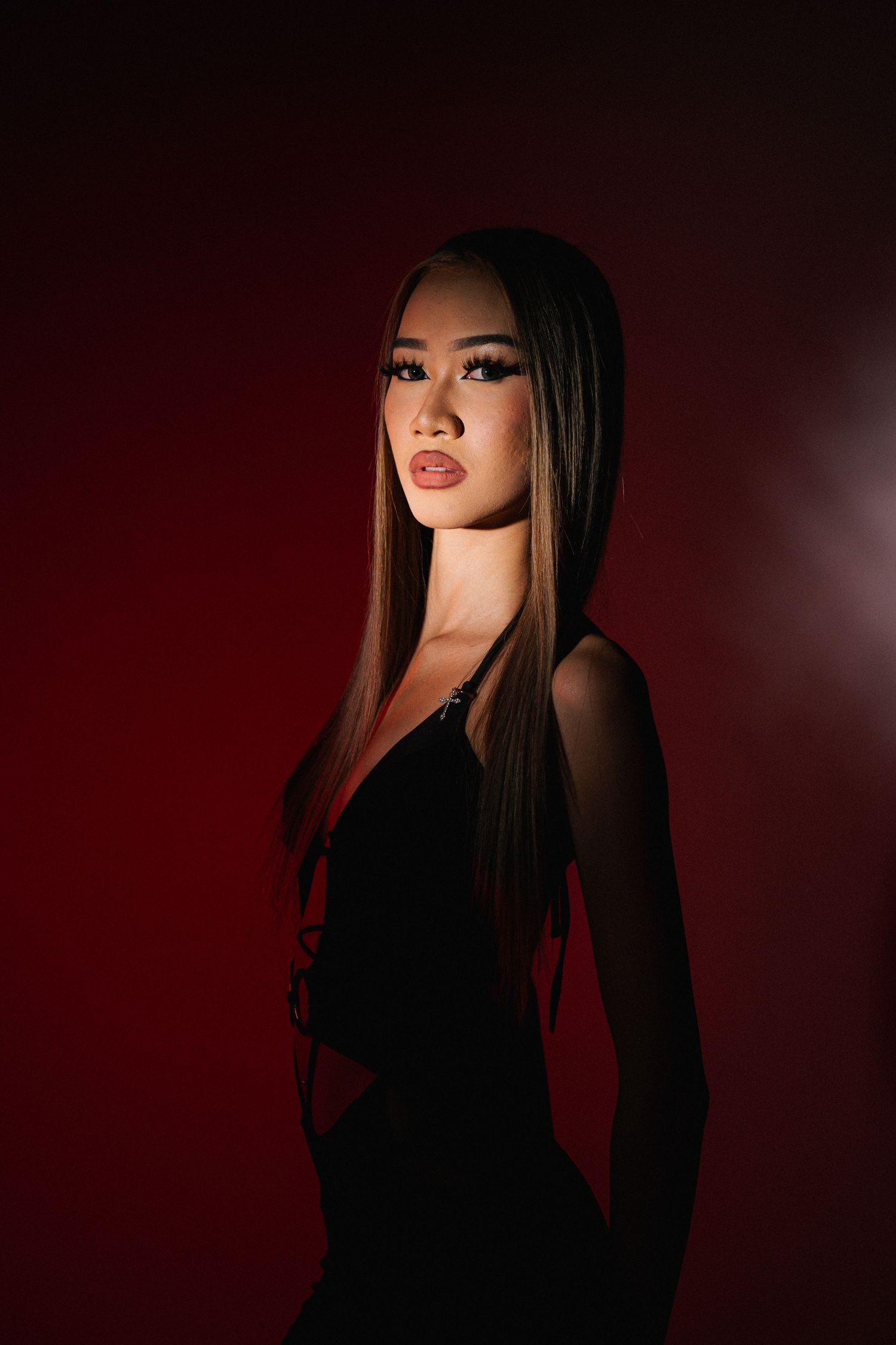 Fashion portrait against dark red backdrop with dramatic lighting and shadows.