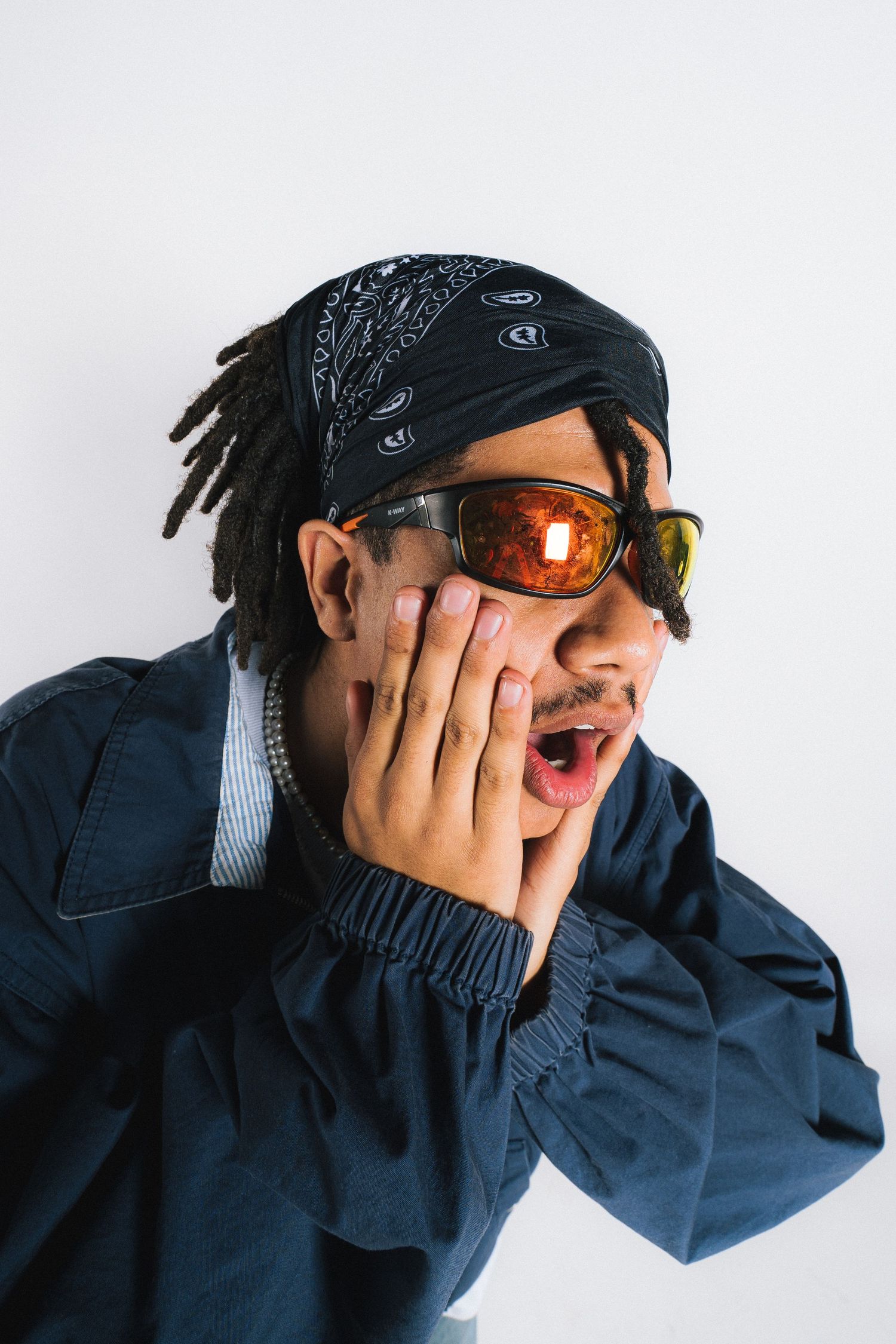 Person in blue jacket and bandana with sunglasses making surprised expression against white background.