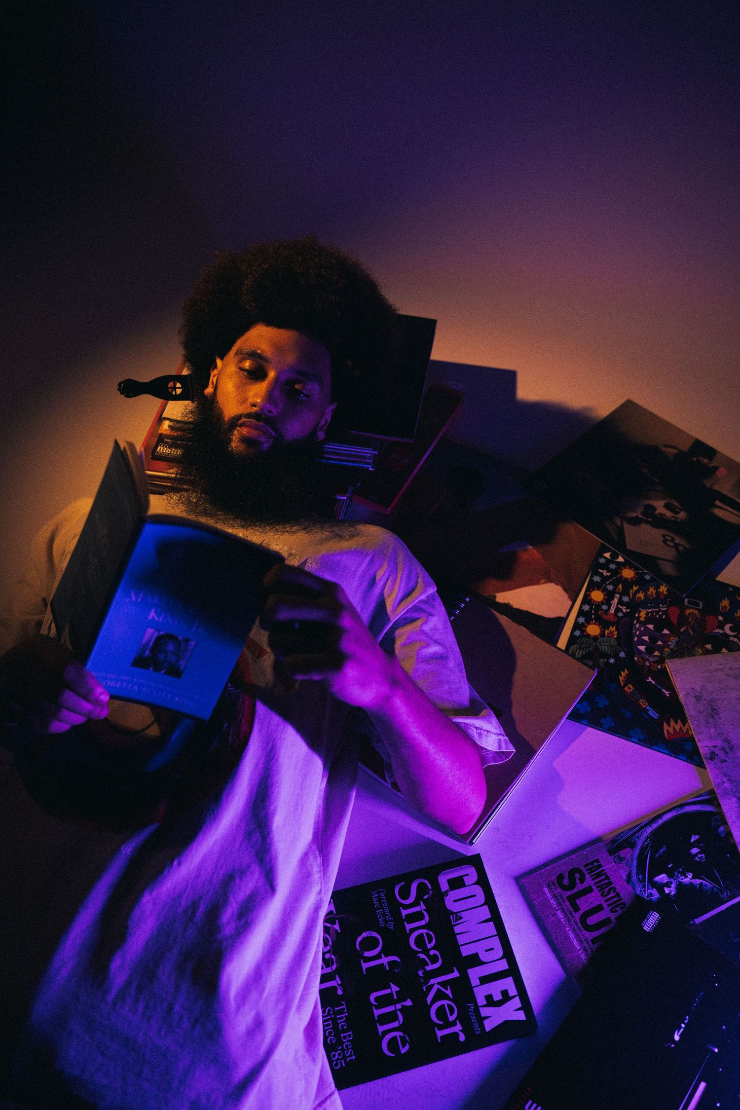 Artist illuminated by purple and orange lighting performs with DJ equipment and vinyl records in a dark studio setting.