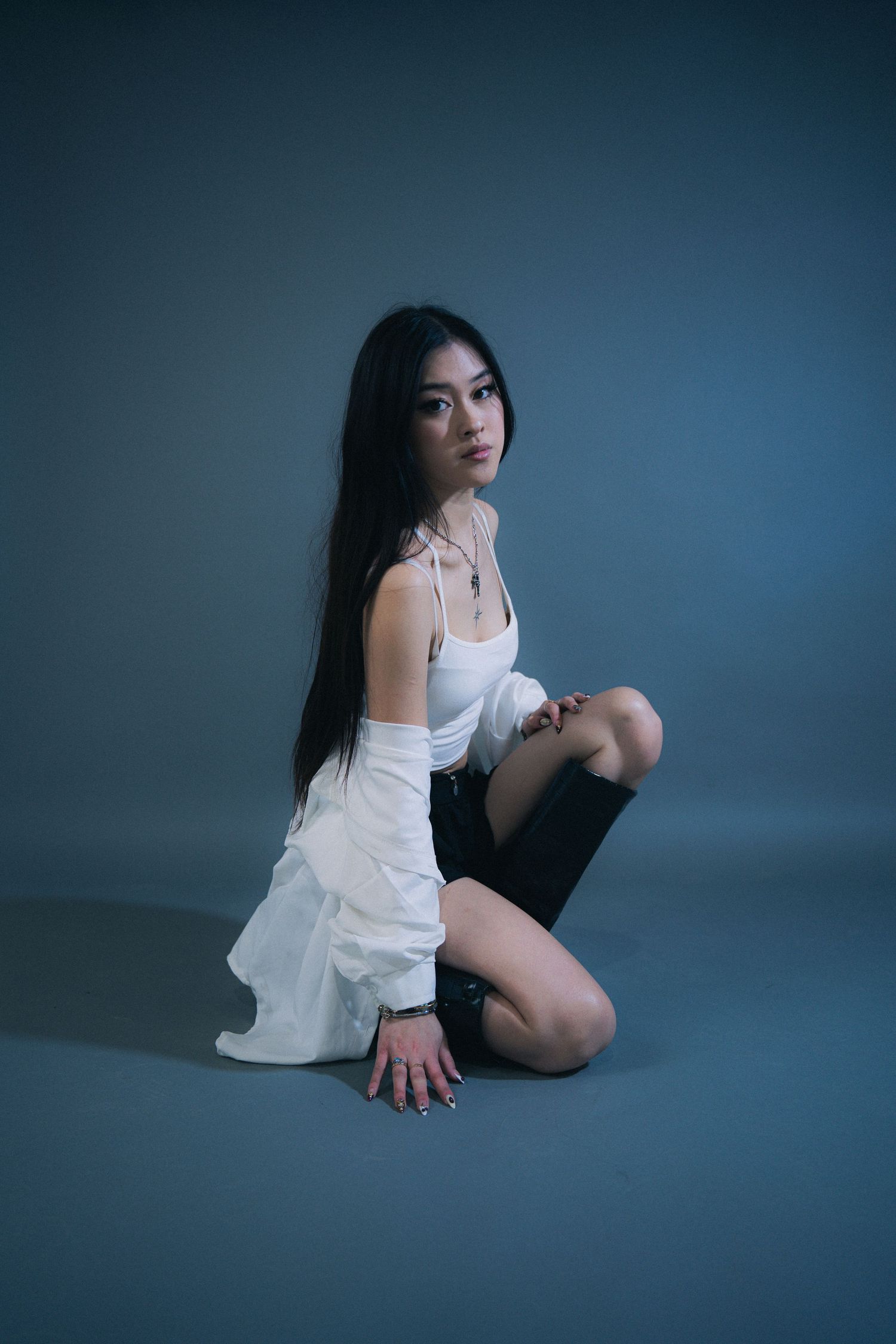 Artistic portrait of a person in white clothing kneeling on dark floor against moody blue background.