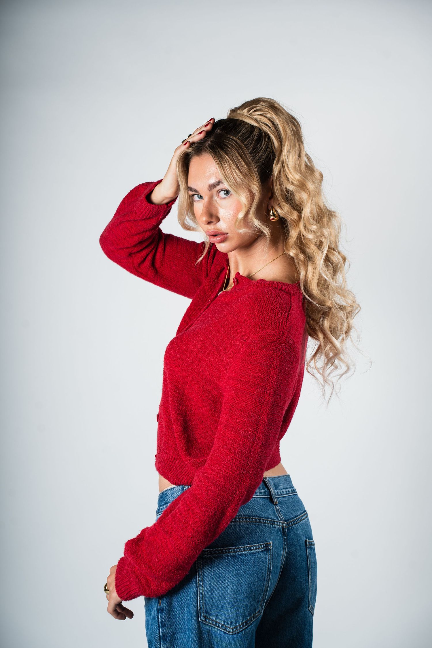 A person in a red knit sweater and blue jeans poses against a light gray background.