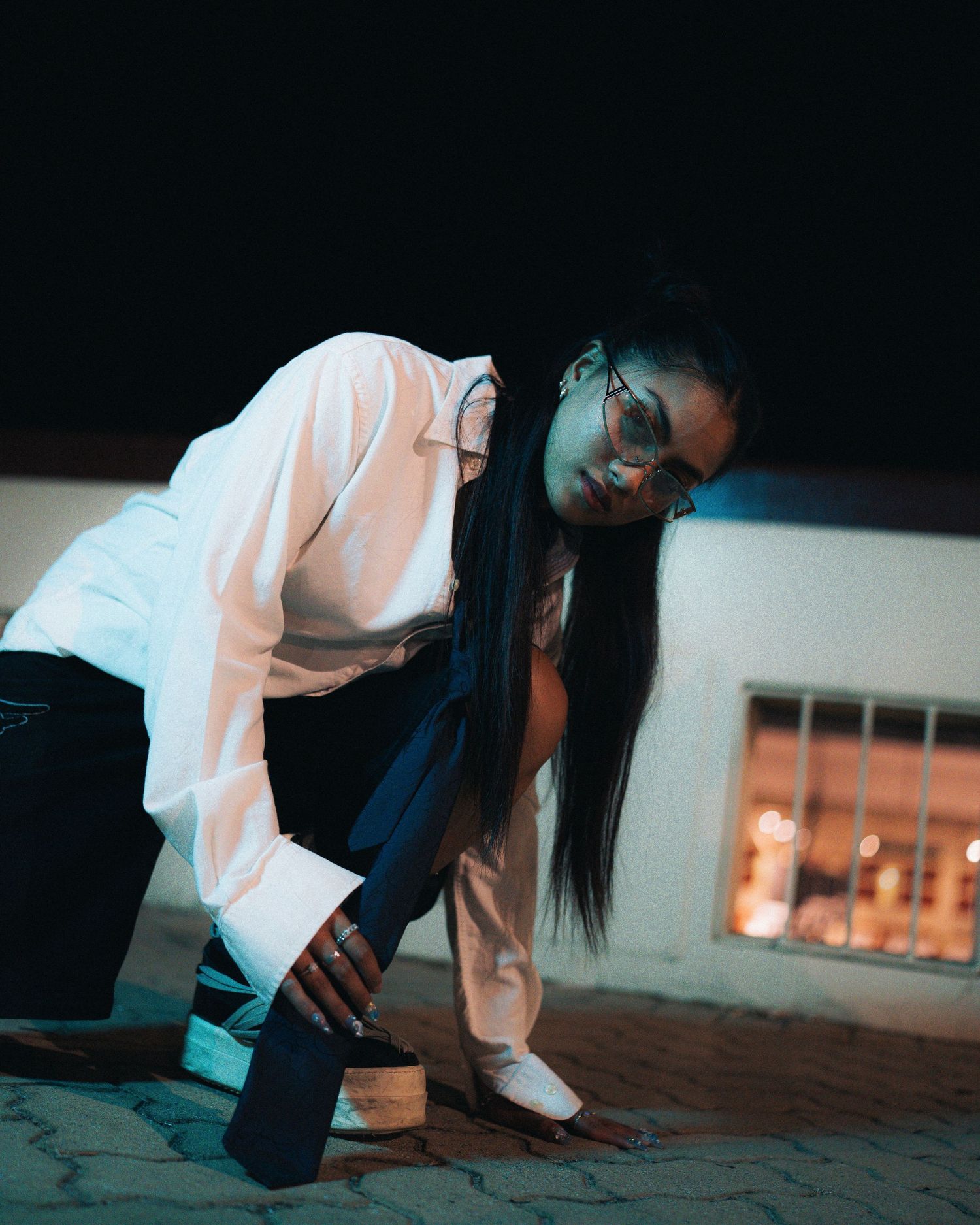 Figure in white shirt and dark pants bends forward in dramatic pose under cool lighting.