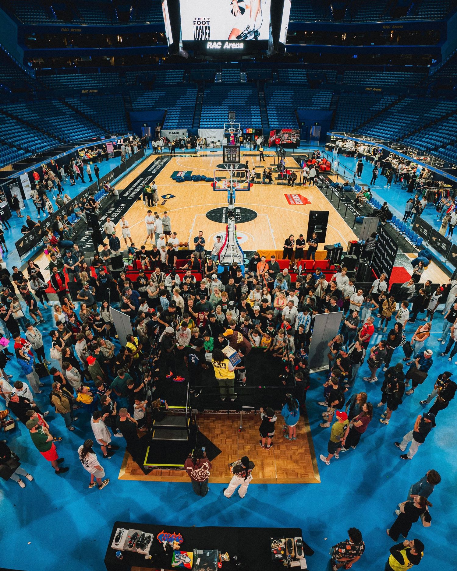 Aerial view of a basketball court event setup with crowds gathered around the perimeter.