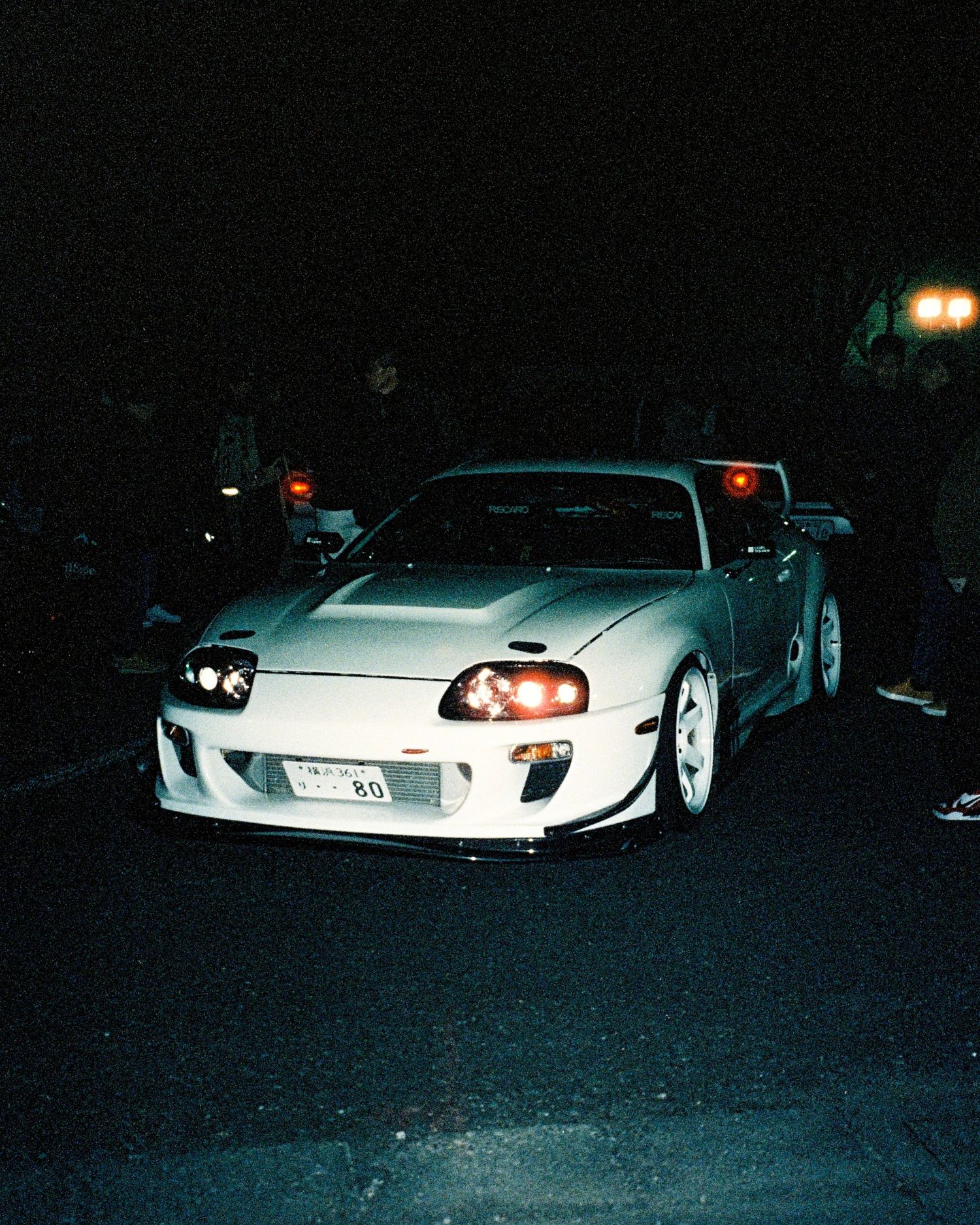 Modified silver Toyota Supra with custom bodykit and headlights photographed at night.