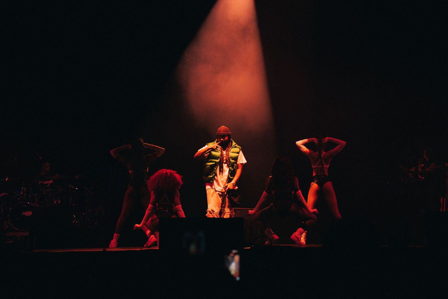 A performer in golden attire stands on stage with dancers in dramatic red lighting during a theatrical performance.