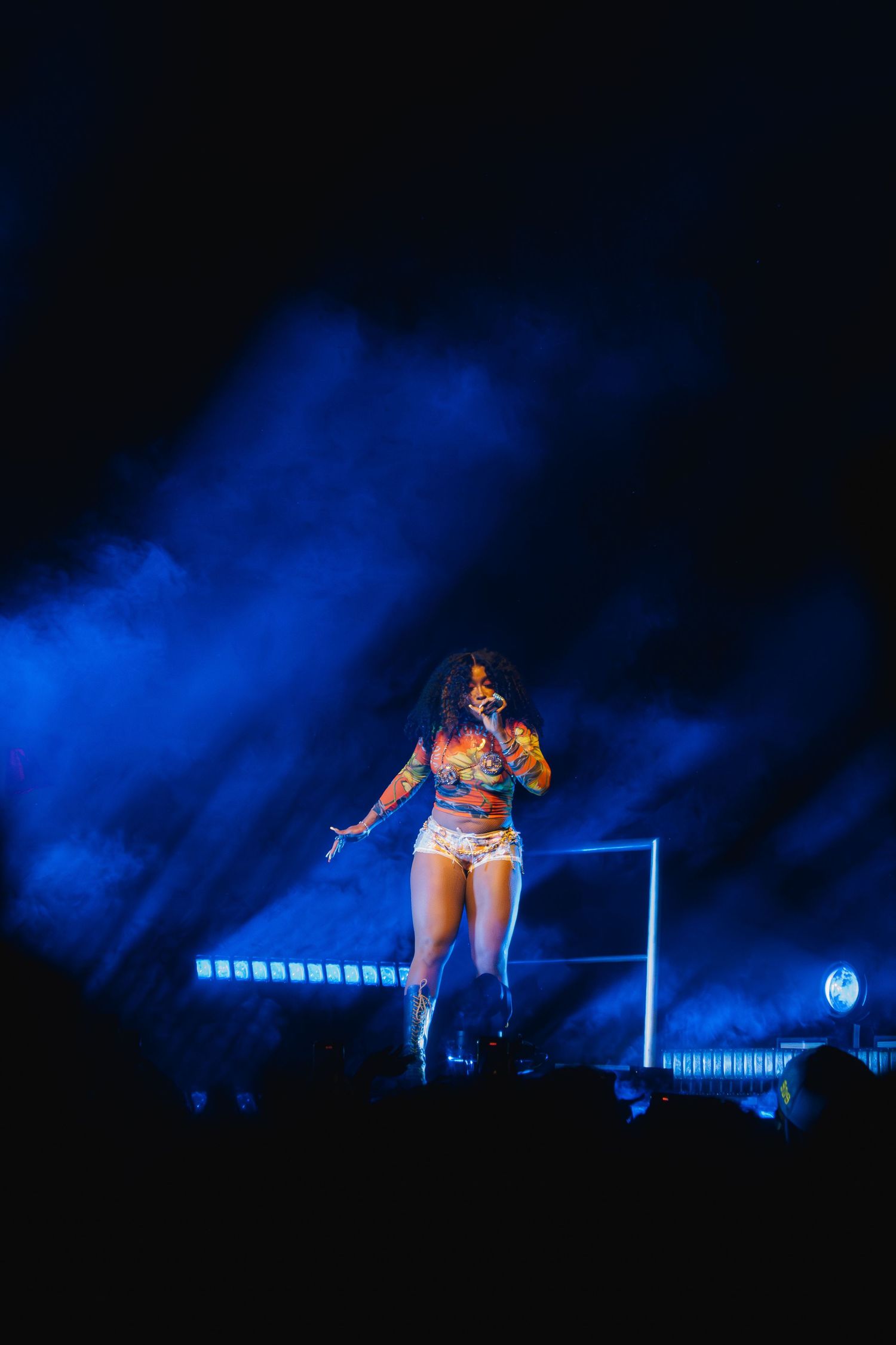Performer on stage in sparkly costume illuminated by dramatic blue stage lighting and smoke effects during concert performance.
