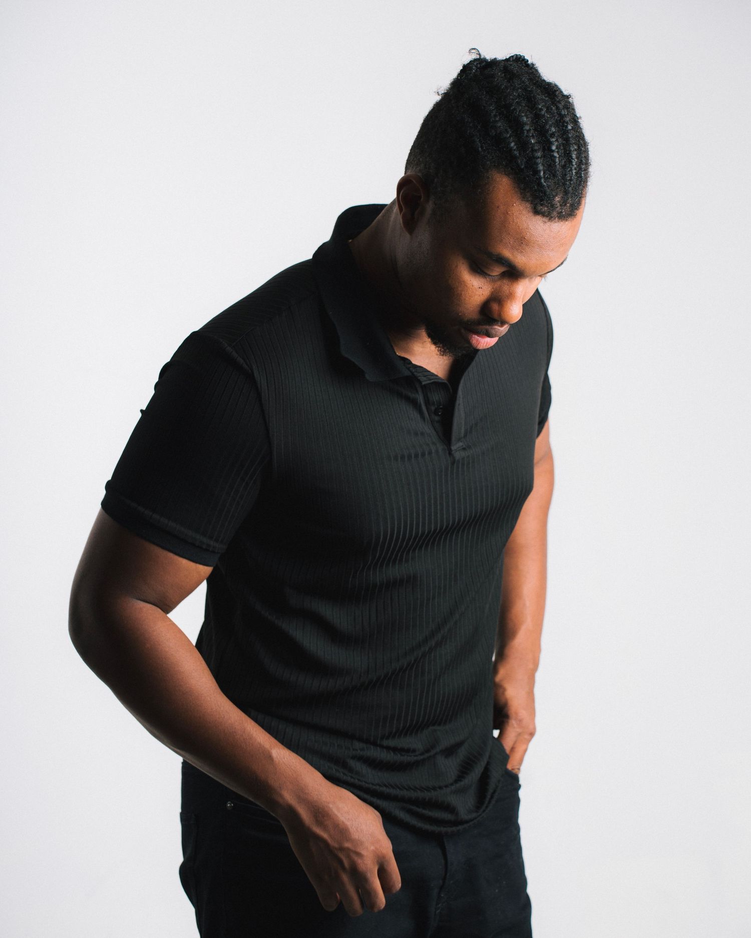 Person wearing black sleeveless shirt posing against white background in dramatic lighting.