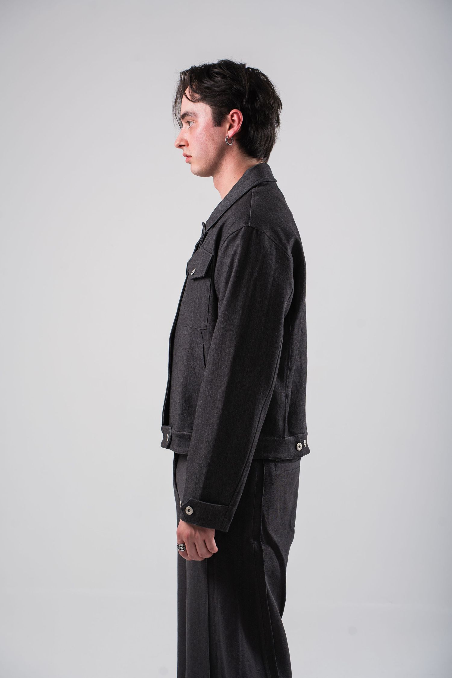 A person wearing a black ankle-length trench coat stands against a white backdrop, shown from multiple angles.