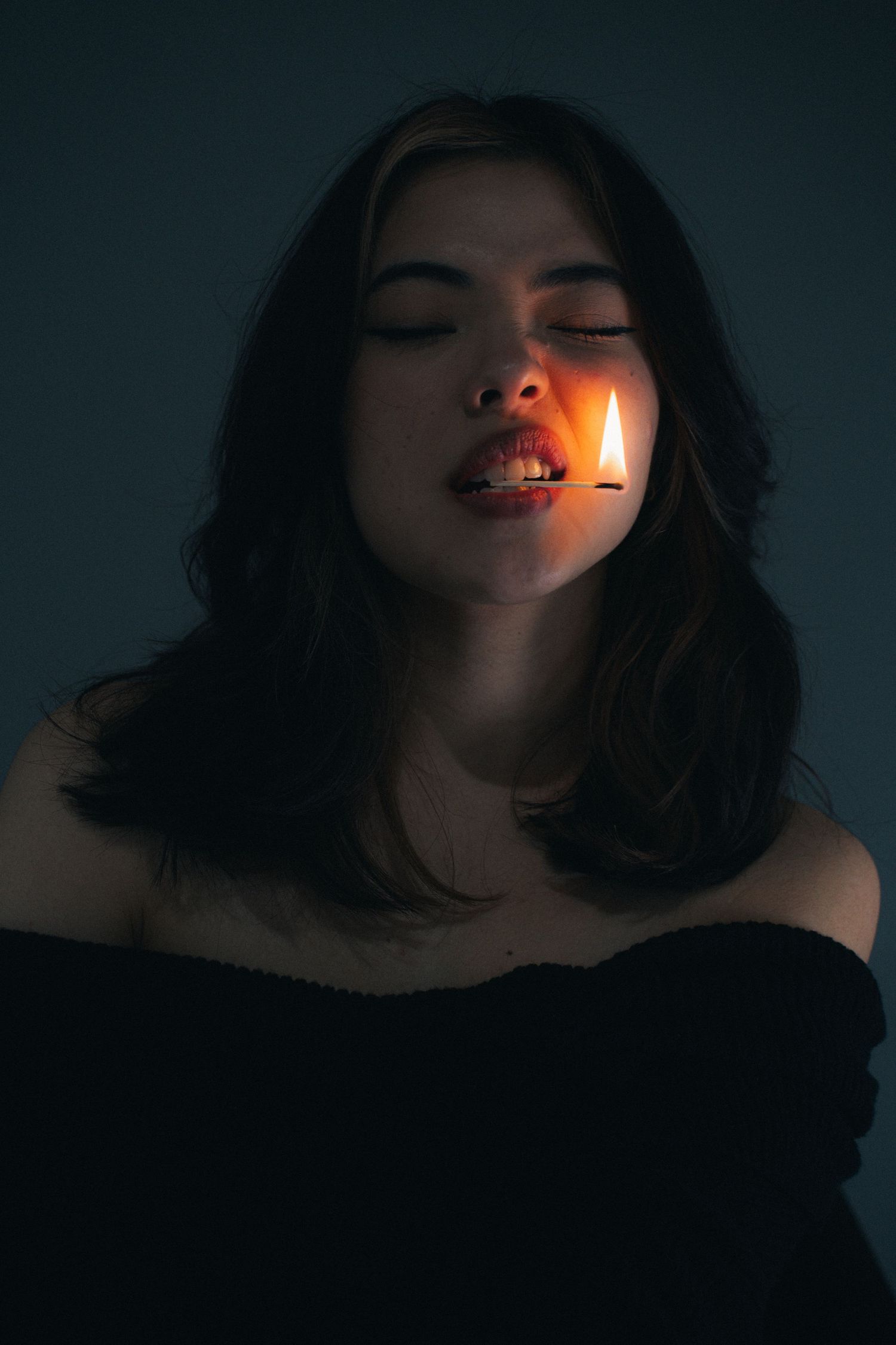 Artistic portrait in dark lighting with candlelight illuminating one side of a face against black background.