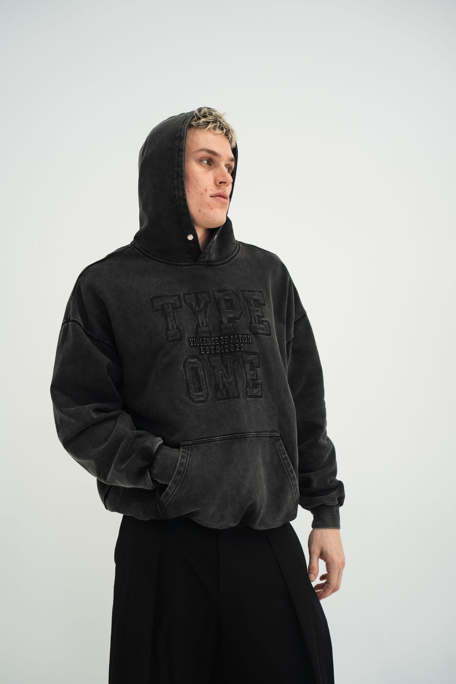 Person in black embossed hoodie and wide-leg pants against white background.