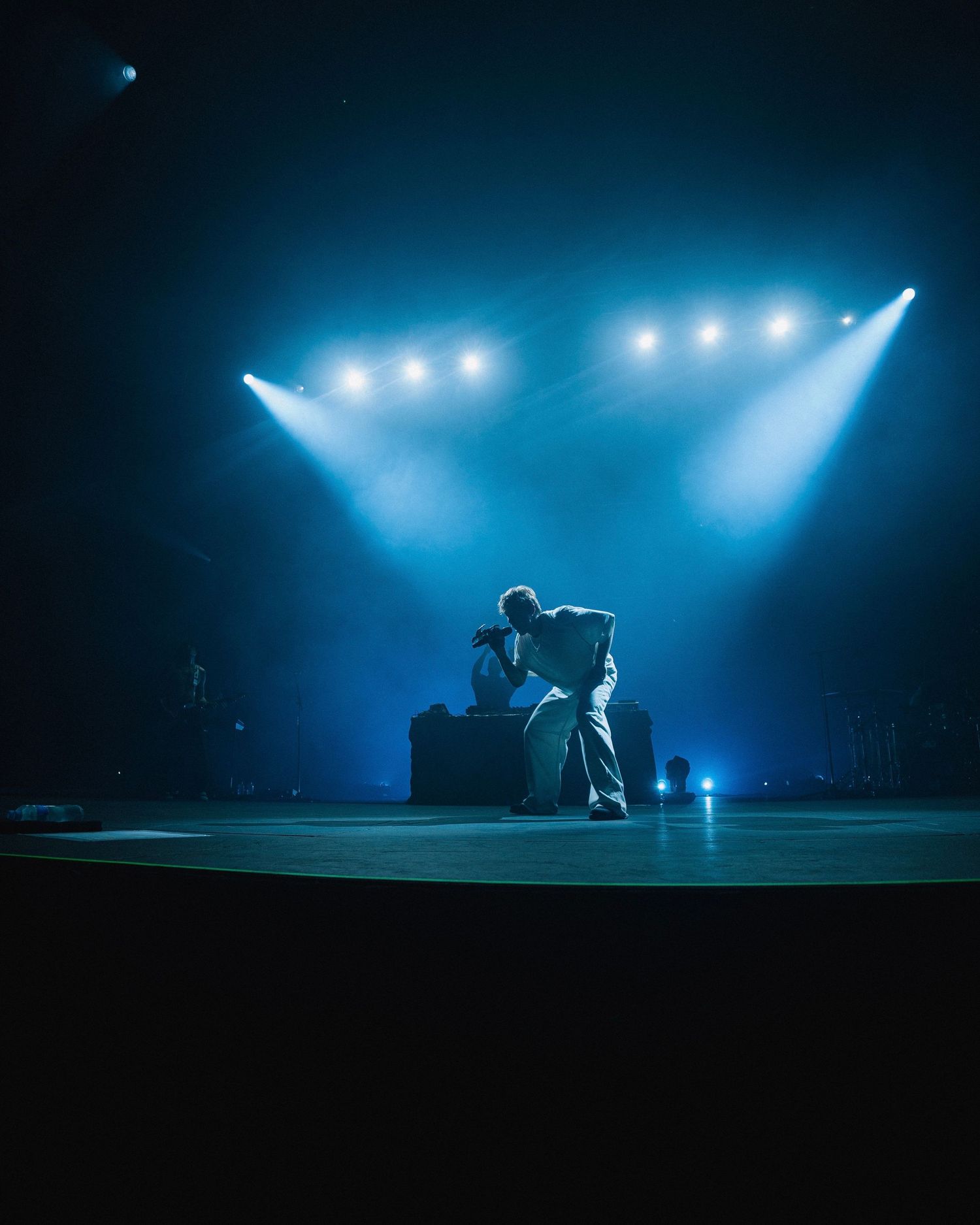 A performer sits alone on stage under dramatic blue spotlights creating a moody atmospheric scene during a live performance.