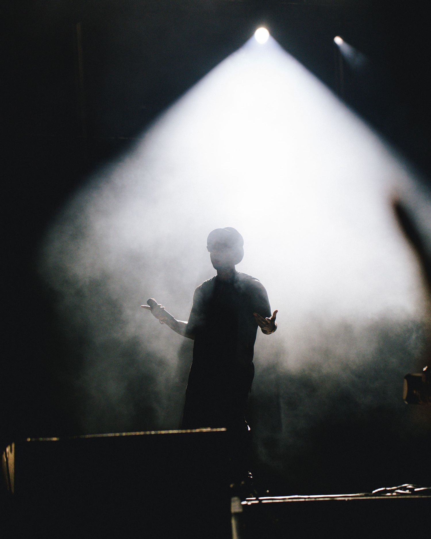 A silhouetted performer stands on stage with dramatic white backlighting and atmospheric fog effects during a show.