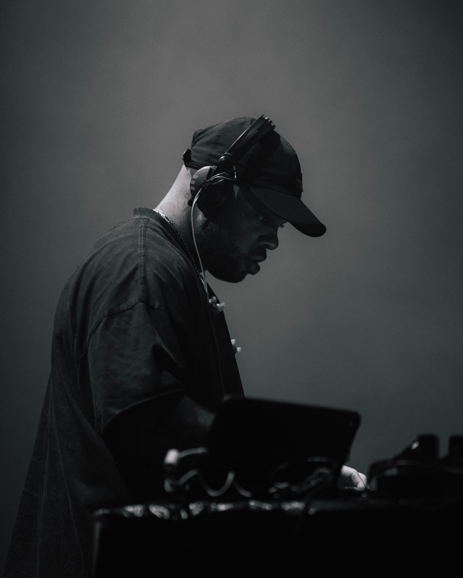 A DJ performs at a mixing console in dramatic black and white lighting, captured in profile against a dark background.