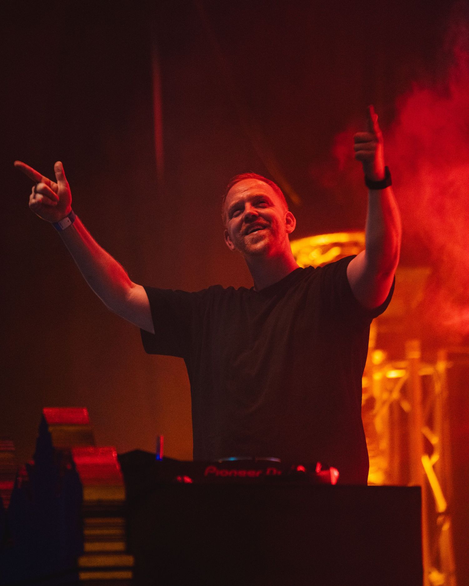 DJ raises arms during performance with dramatic red and orange lighting effects.