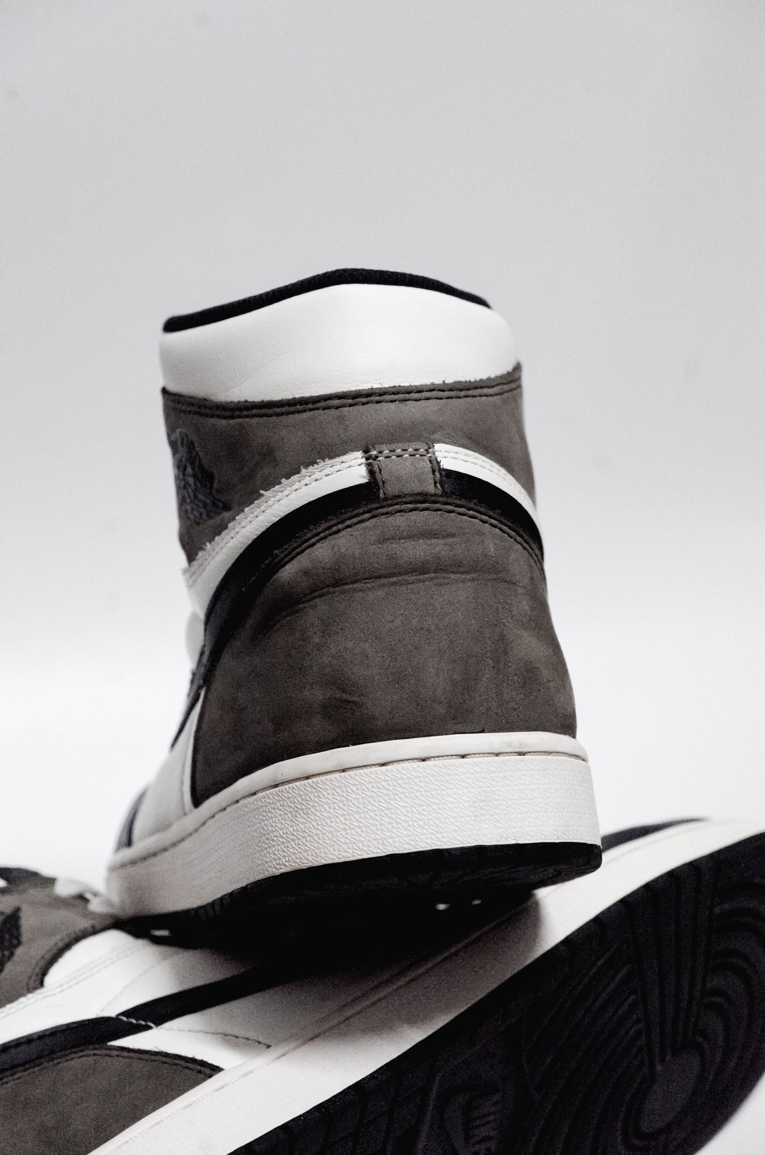 Close-up of a classic Air Jordan 1 sneaker in grey and white leather with black trim against light background.