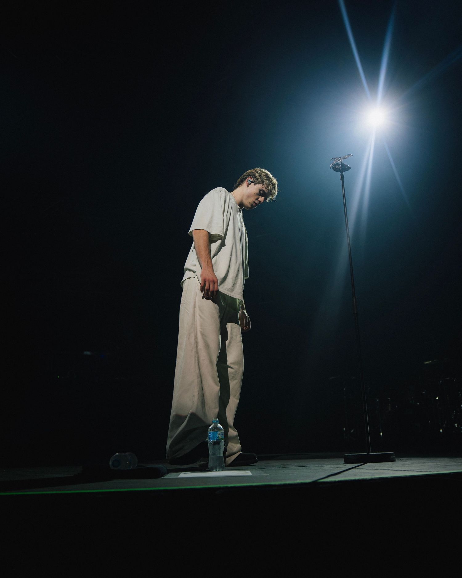 A solo performer stands in spotlight on a dark stage with dramatic lighting against a deep blue background.