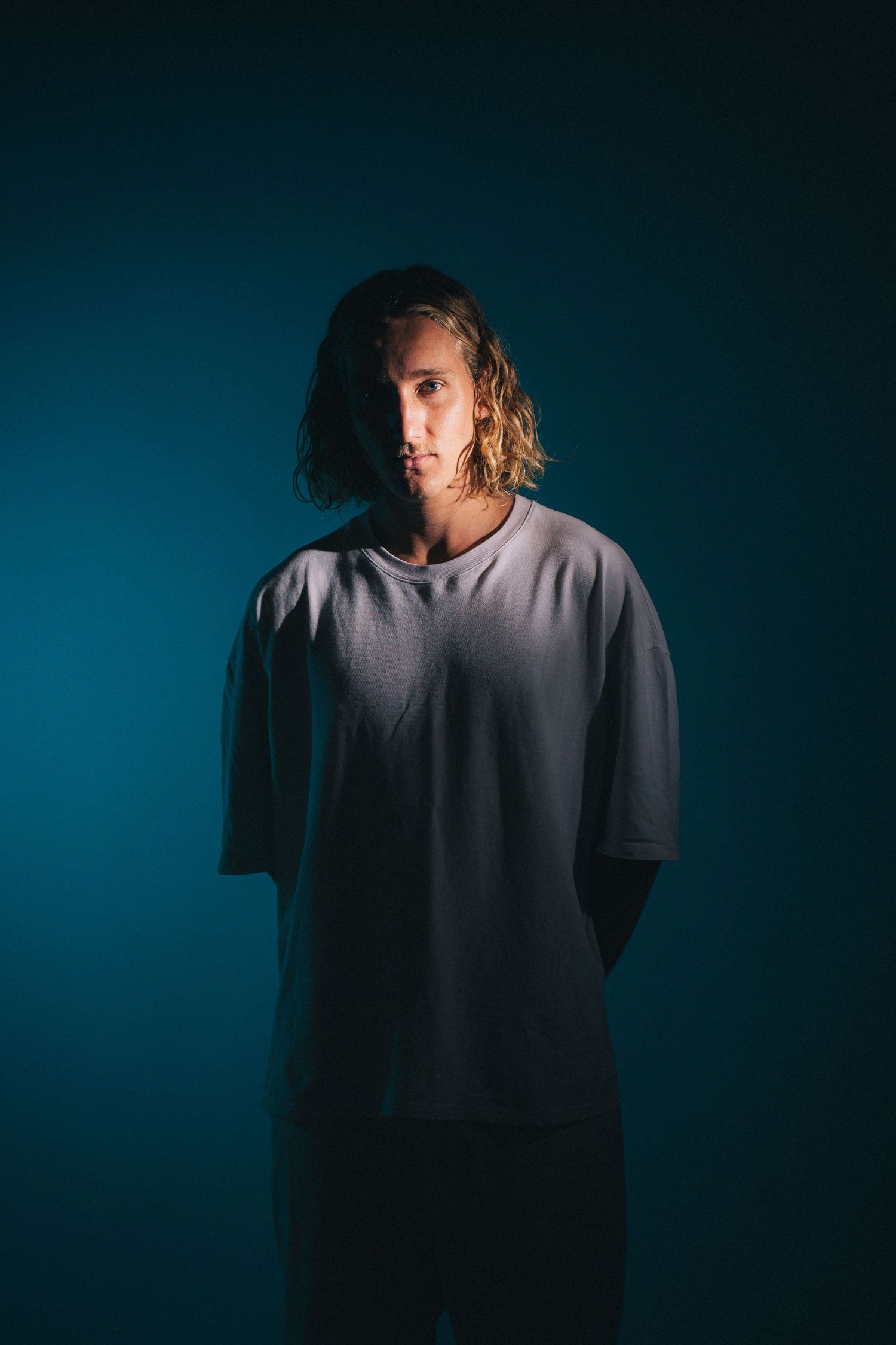 Studio portrait against blue background featuring person in oversized gray t-shirt.