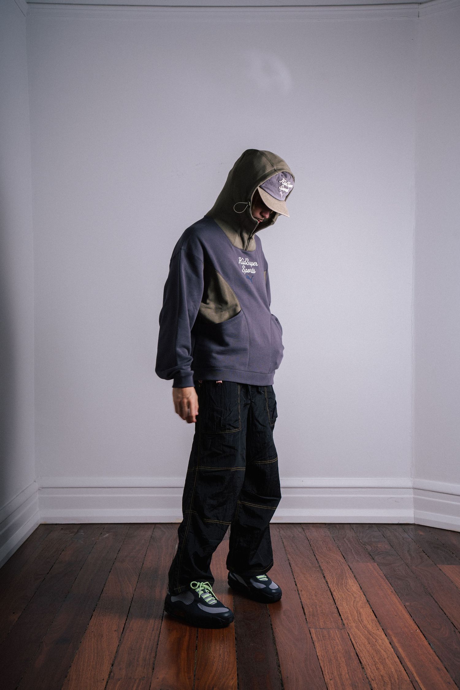 Person in oversized hoodie and baggy pants stands against white wall.
