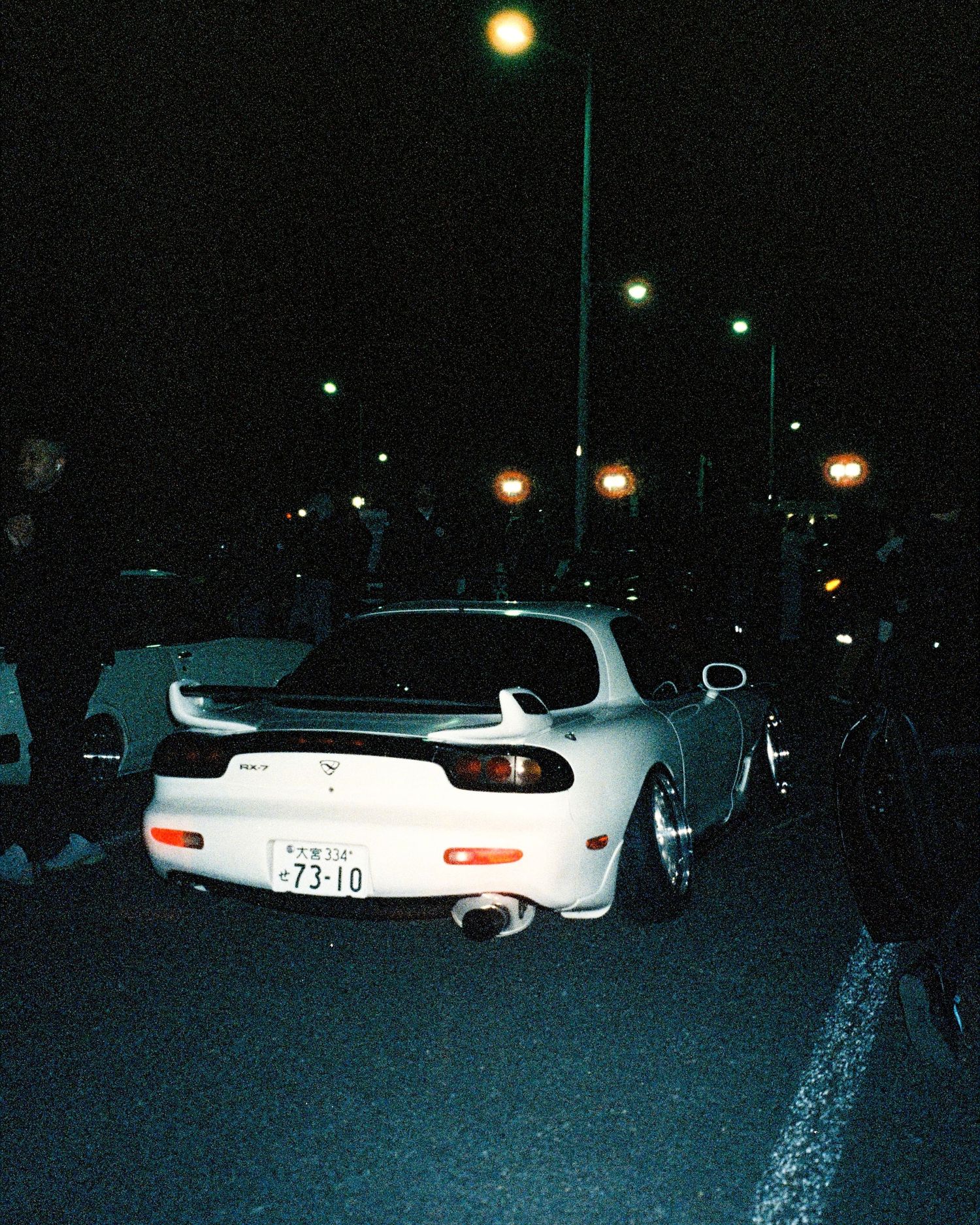 White Mazda RX-7 photographed at night in parking lot with street lights.