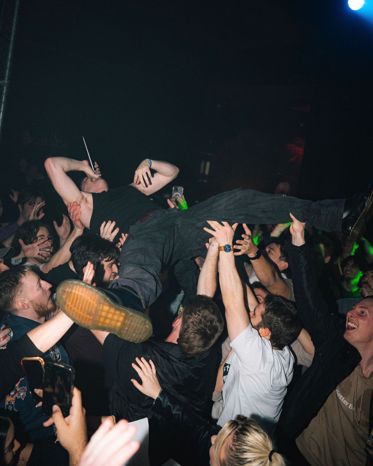 Energetic crowd surfing moment at a dimly lit concert venue with hands raised in support.