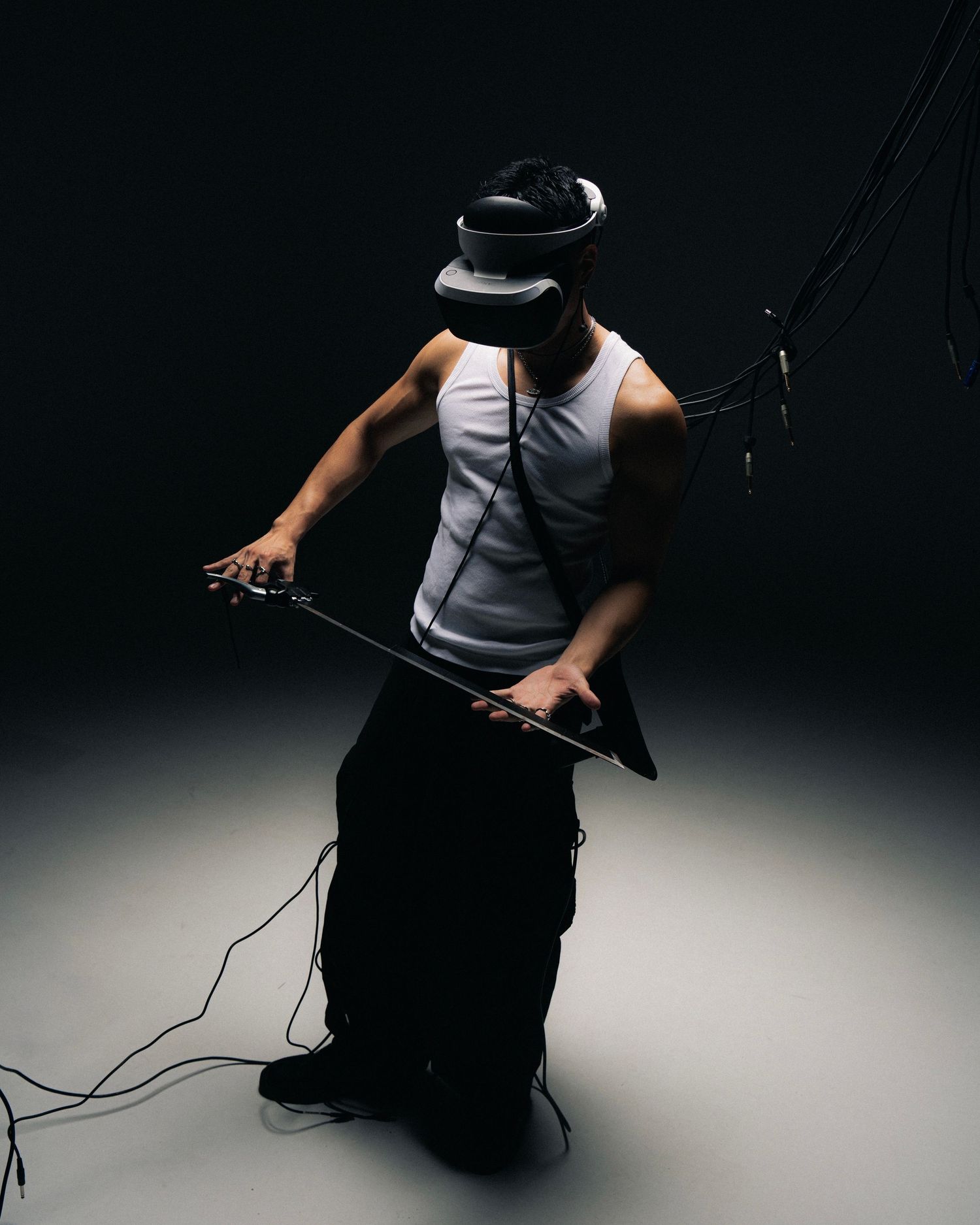 Person in dark attire holds gaming controller while kneeling against dramatic black backdrop with spotlight effect.
