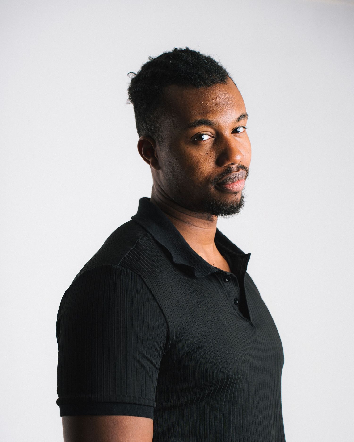 Professional studio portrait of a person in a black polo shirt against a white background.