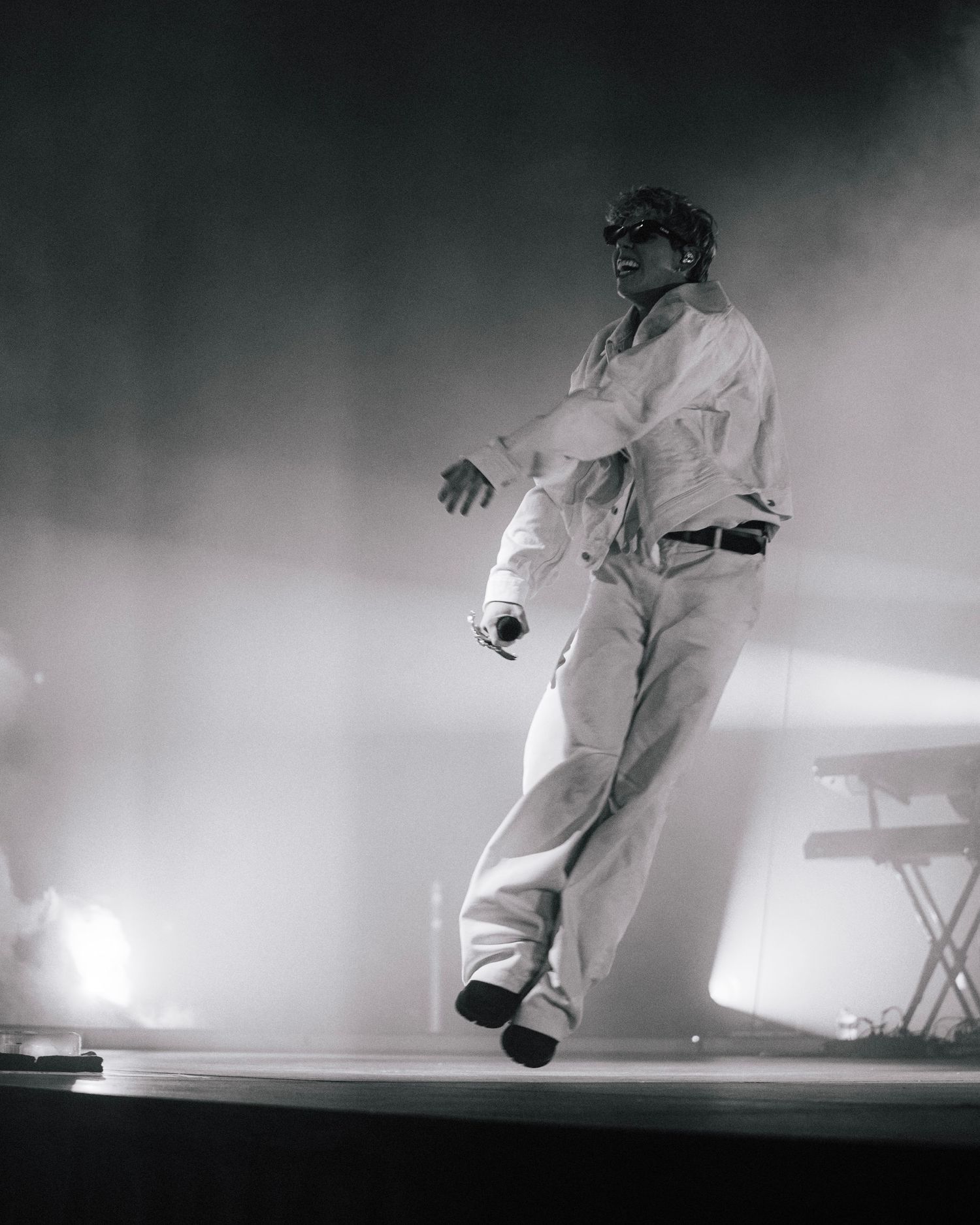 A performer in an all-white outfit appears to be levitating on a smoky stage during a dramatic concert performance.