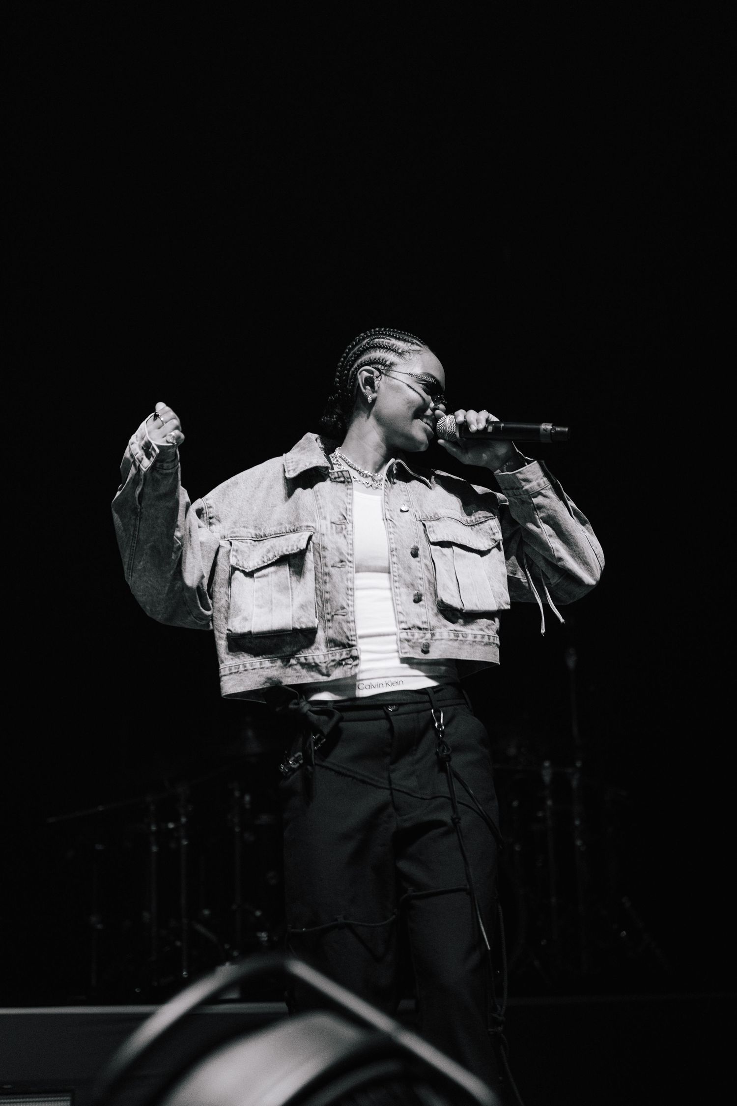 A performer in a denim jacket sings passionately into a microphone on stage in black and white photography.