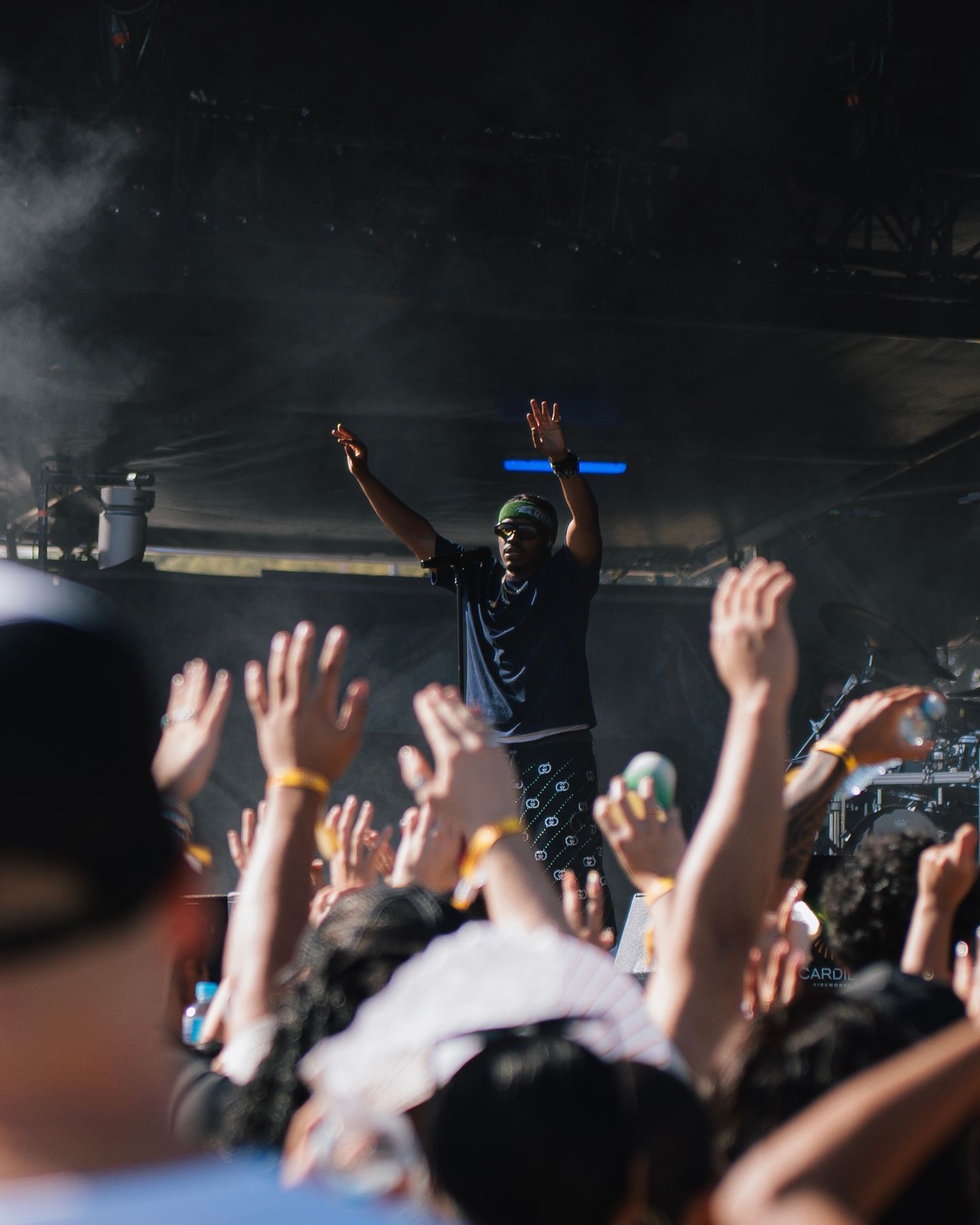 Concert audience raises hands in excitement as performer gestures from stage in dark venue.