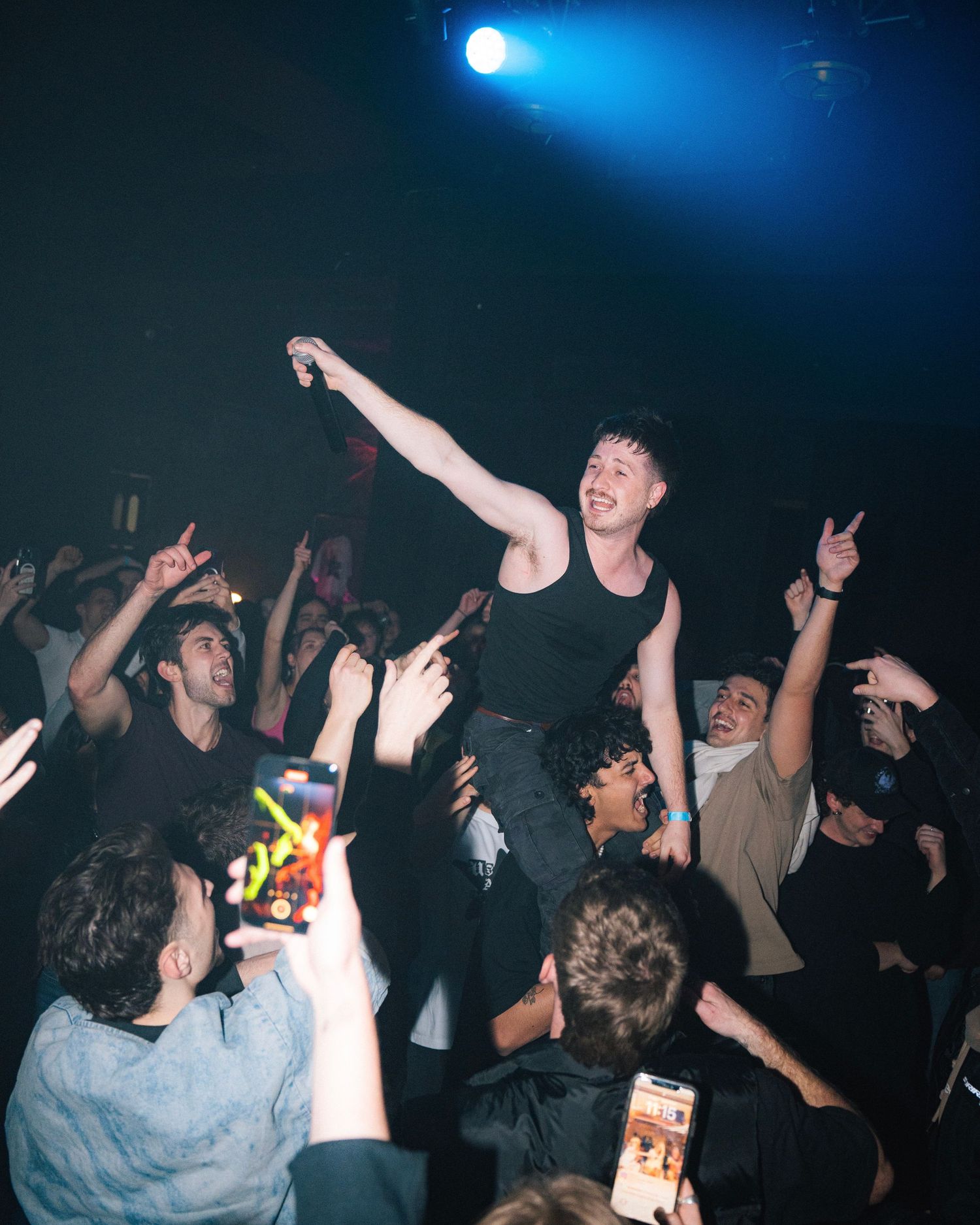 Energetic crowd surfing moment captured during concert with blue spotlight illuminating the scene.