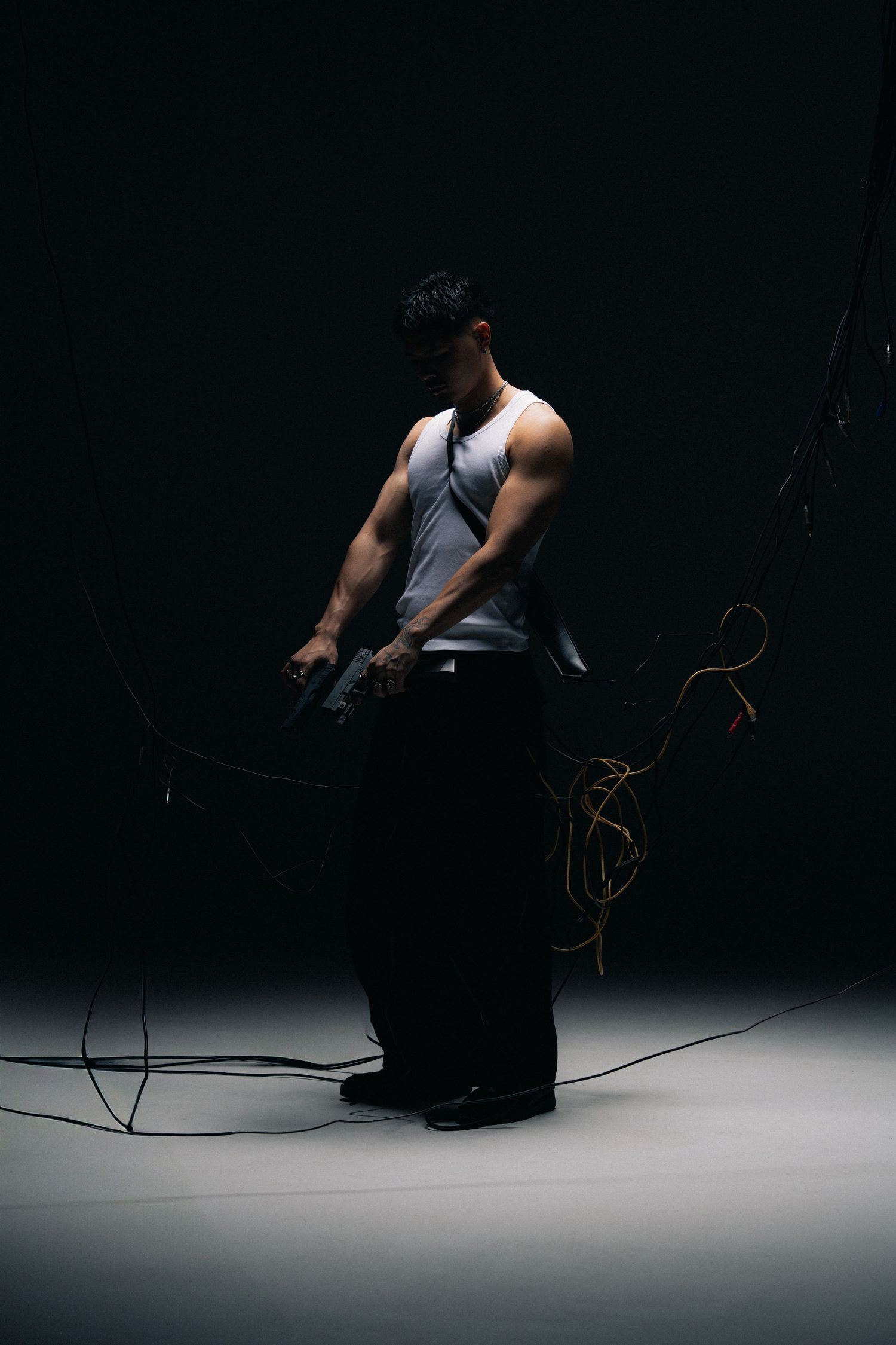 Athletic person in a white tank top performs tricep pulldowns in a dimly lit gym against a dark background.