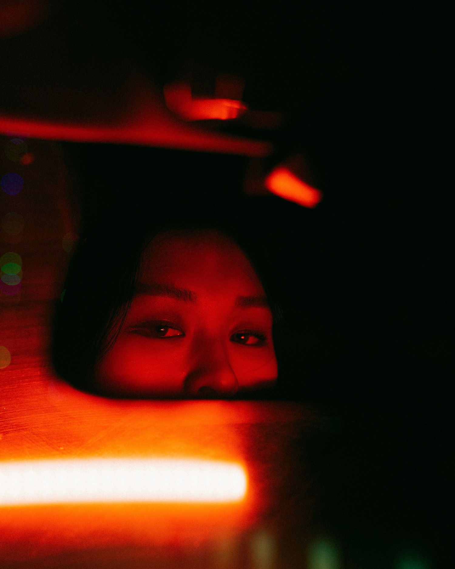 A dark moody portrait illuminated by red lighting with dramatic shadows and reflections.