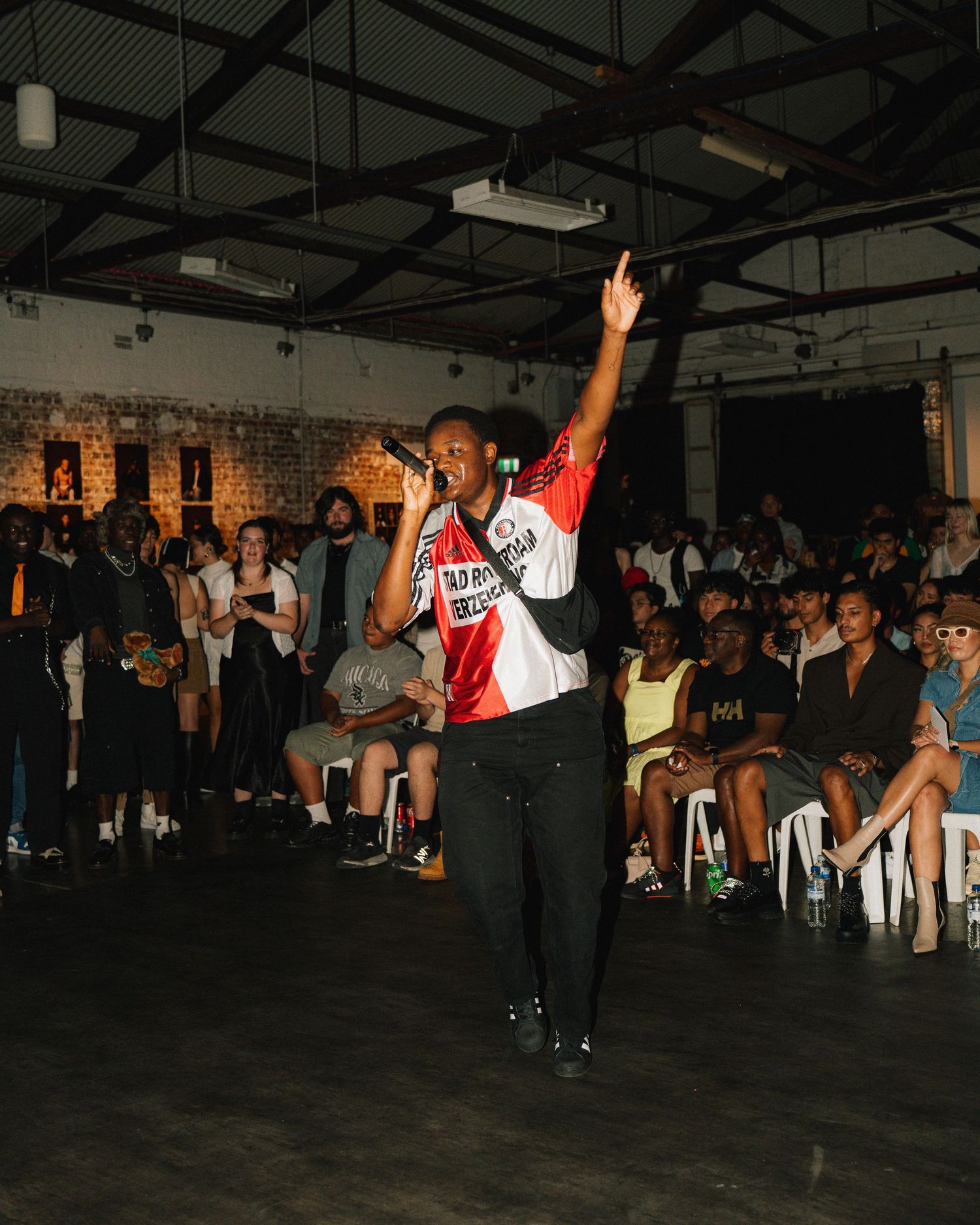 Energetic performer on stage during an indoor event with audience seated in background.