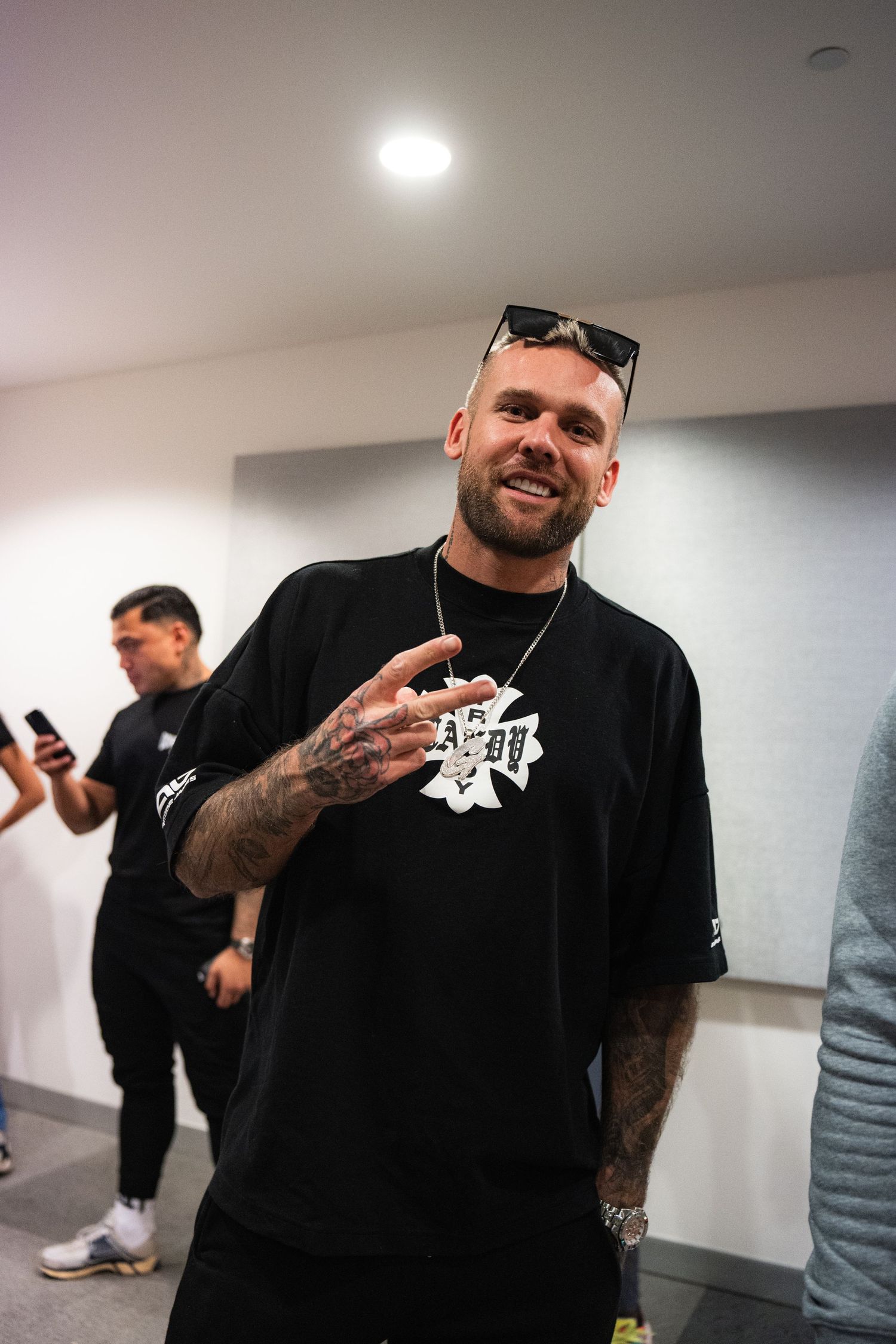 Candid indoor shot of a person in black t-shirt with tattoos making hand gesture.