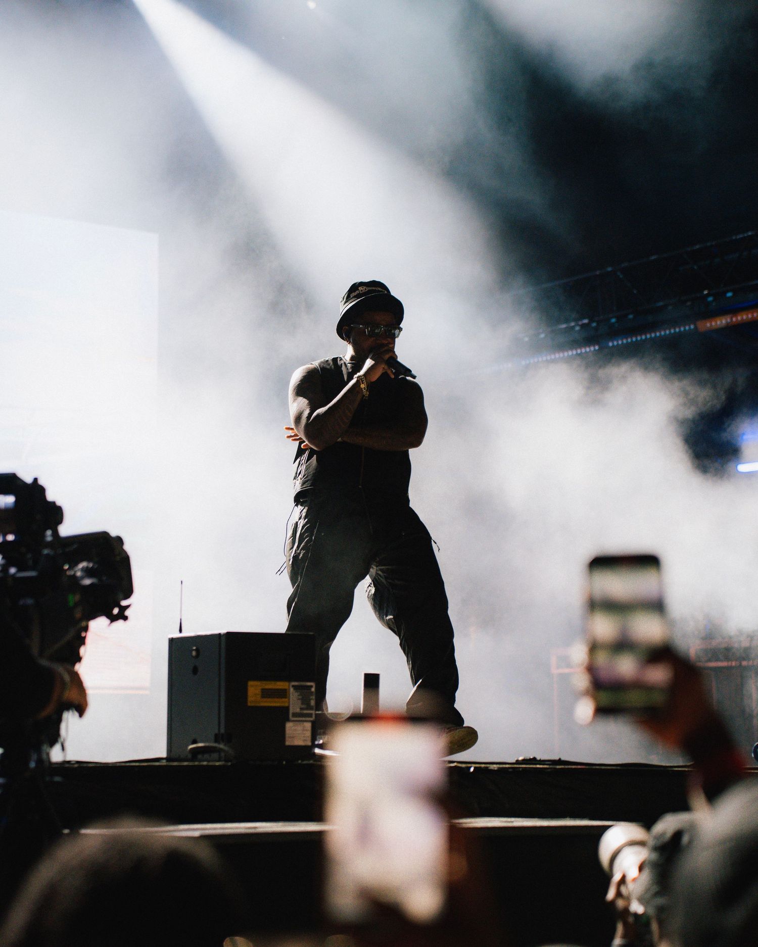 Performer on stage silhouetted against dramatic white spotlights and fog during a concert performance.