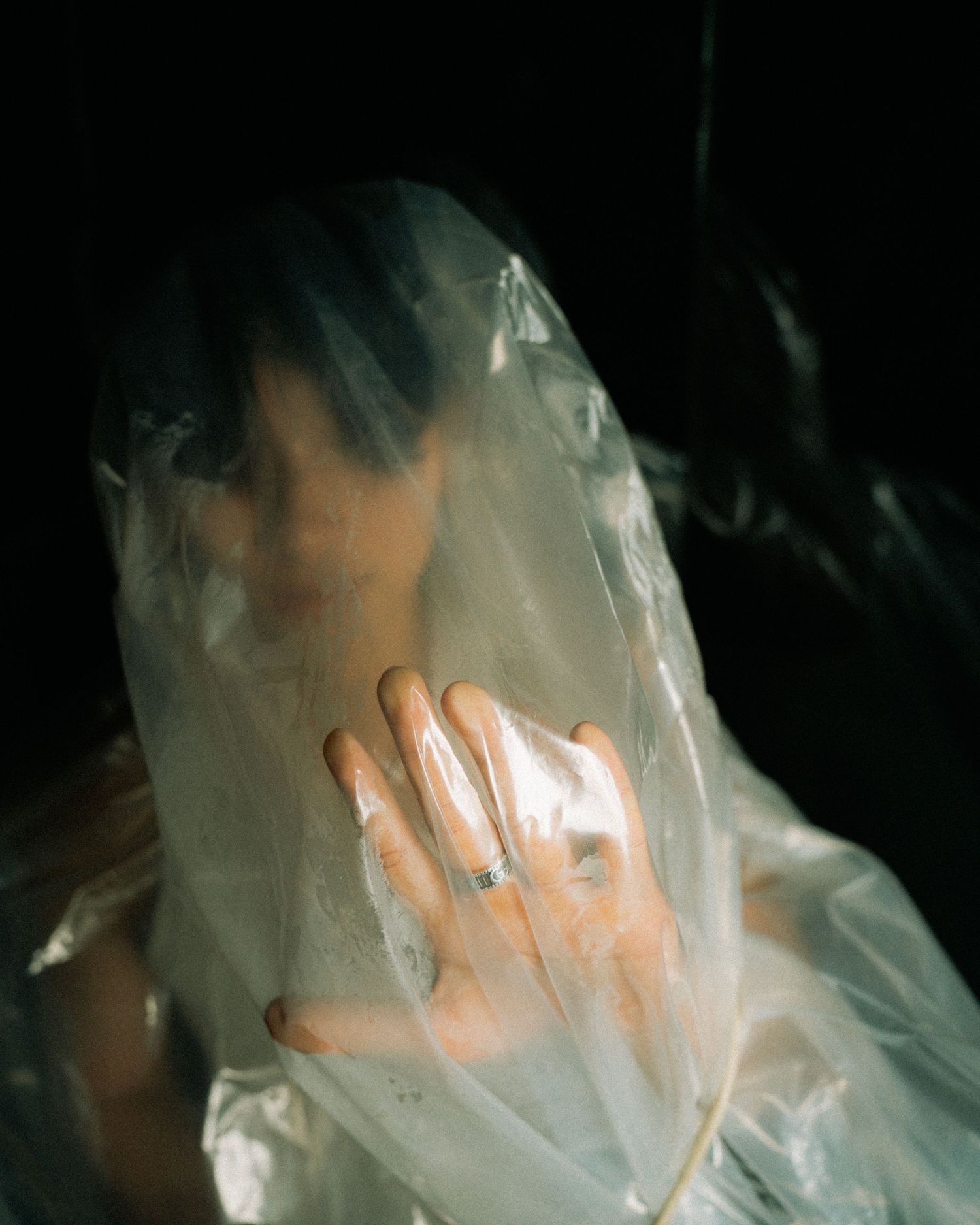 A hand covered by translucent plastic material creates an ethereal effect against a dark background.