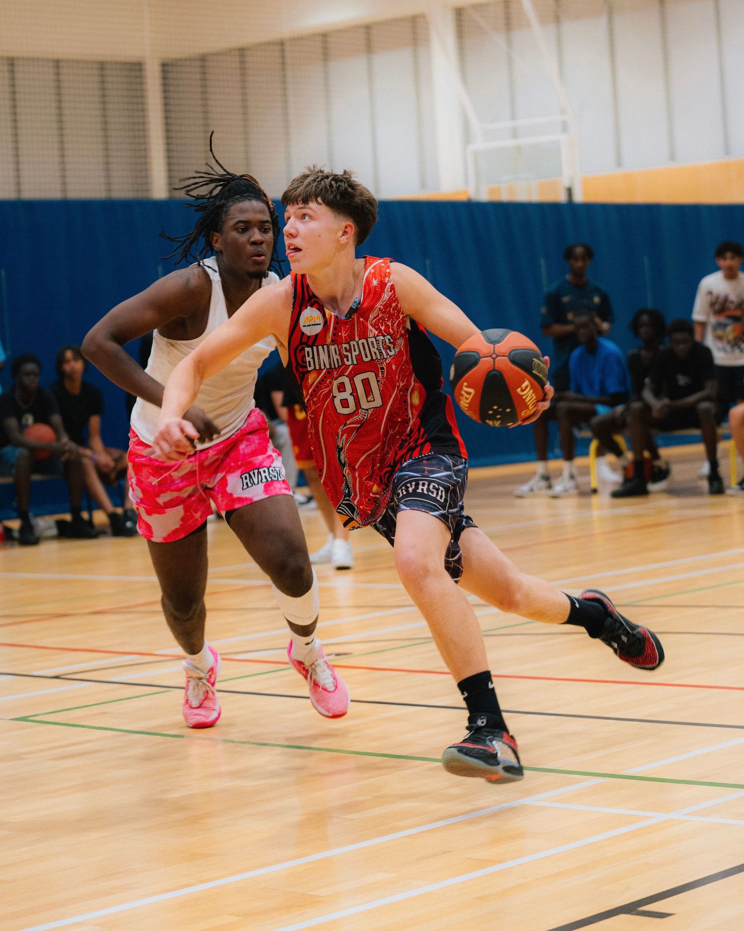 Basketball players in orange and pink uniforms competing intensely on an indoor court during a game.