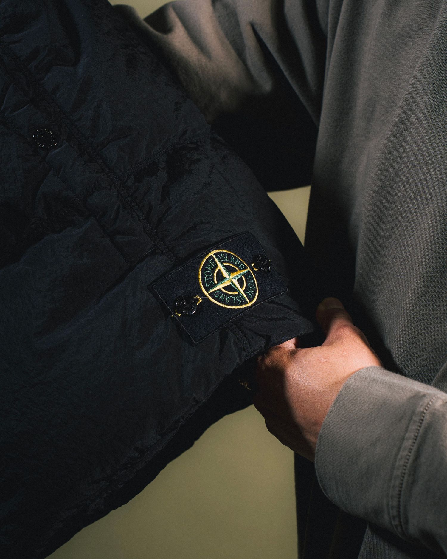 Close-up detail of black jacket showing circular Stone Island compass patch logo.