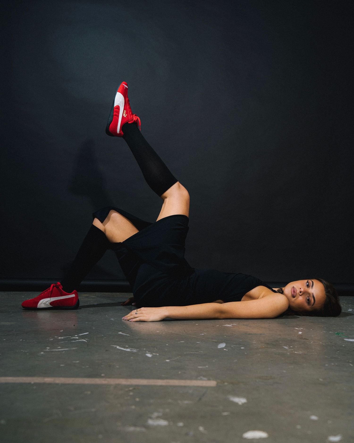 Athletic pose showcasing red sneakers against dark background with dramatic lighting.