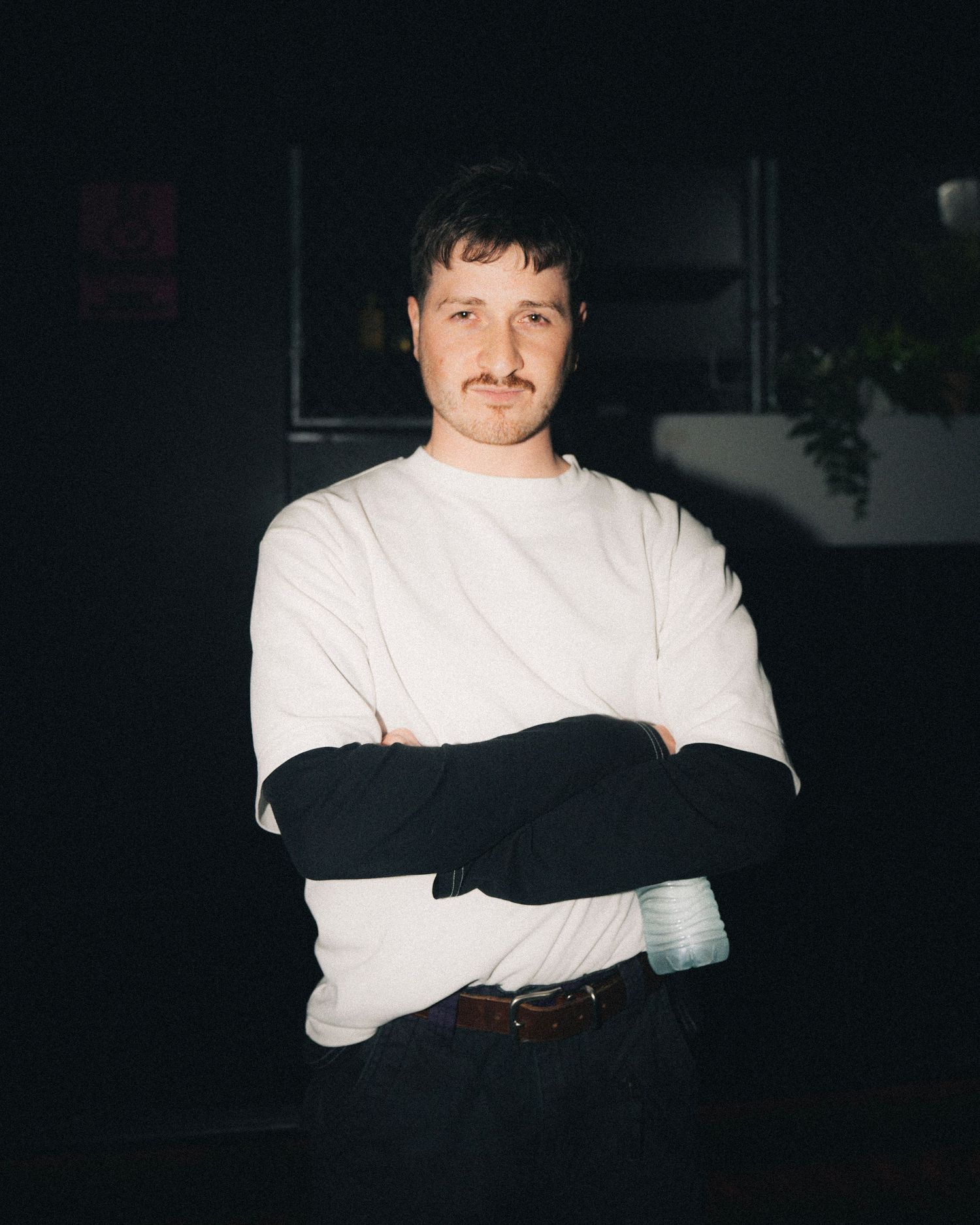 Person in white sweater with black sleeves standing against dark background.
