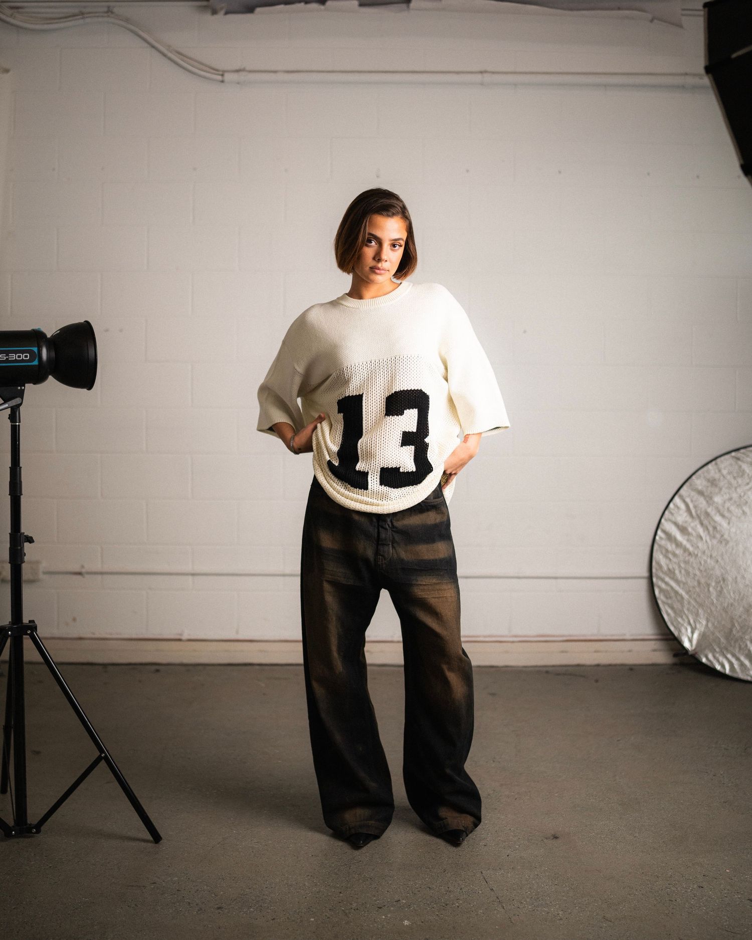 Studio photo shoot setup with person wearing white jersey with number 13 against white backdrop.