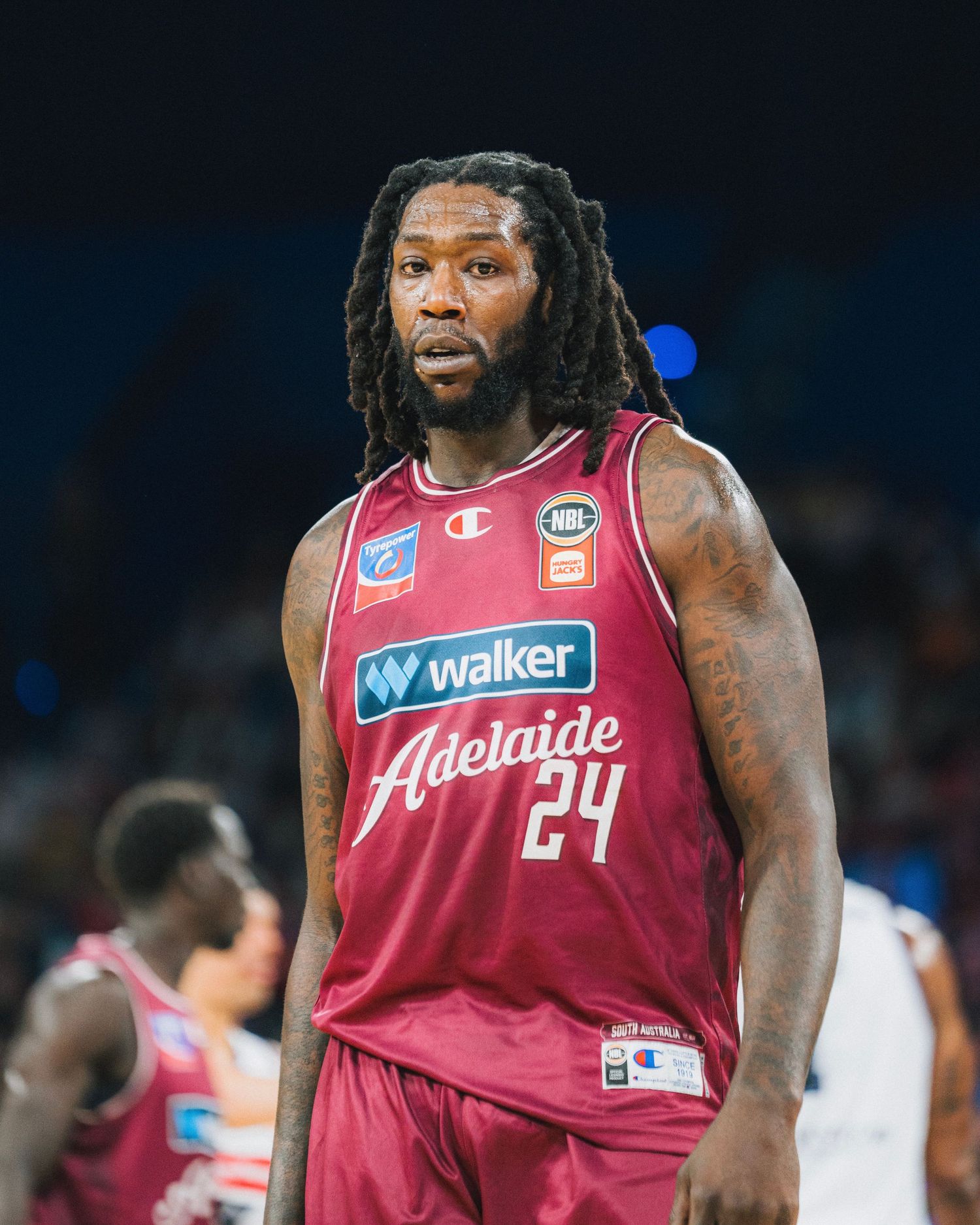 Basketball player in red Adelaide jersey stands on court during game.