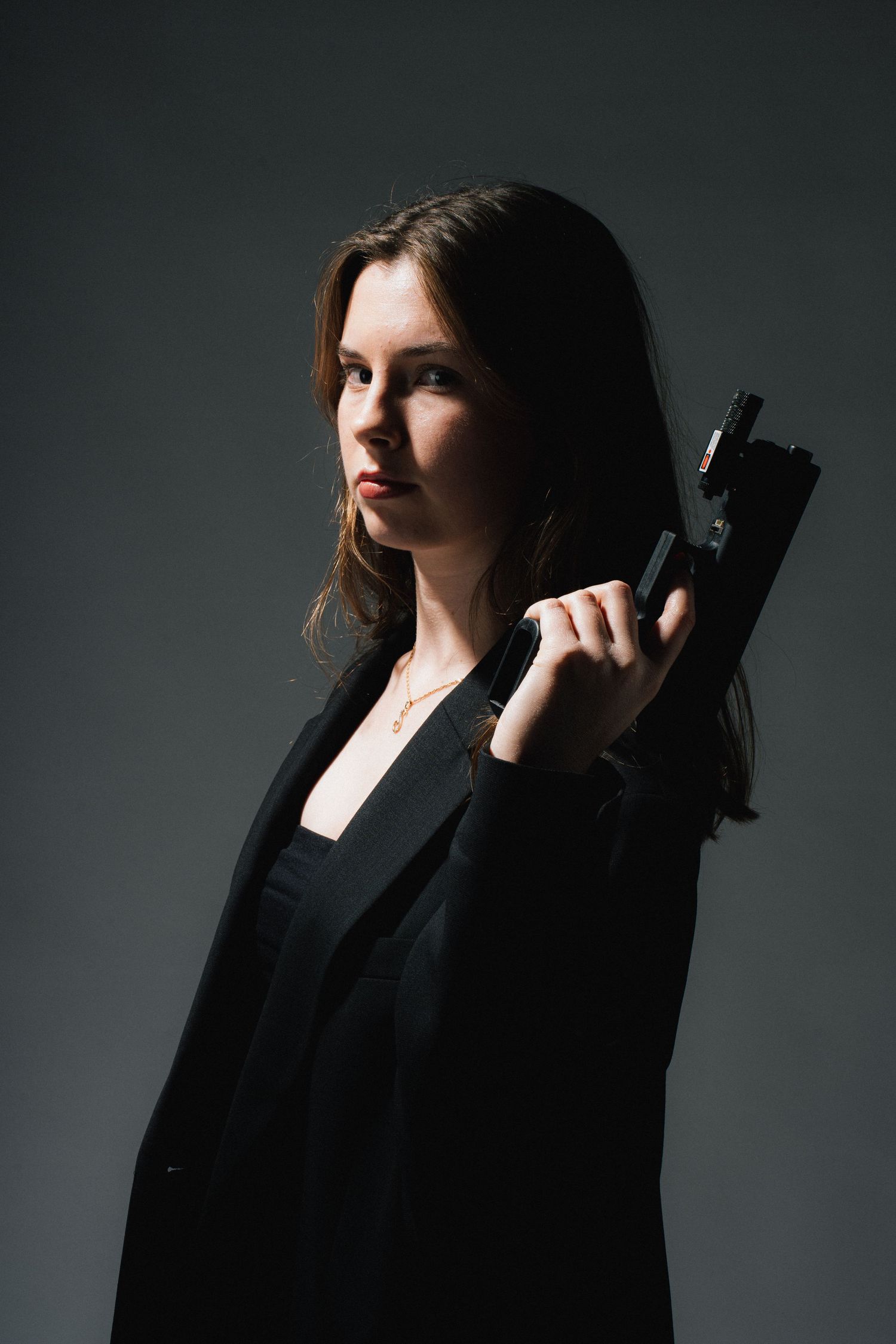 Woman in black outfit holding a gun against dark background in dramatic sequence of moody studio portraits.