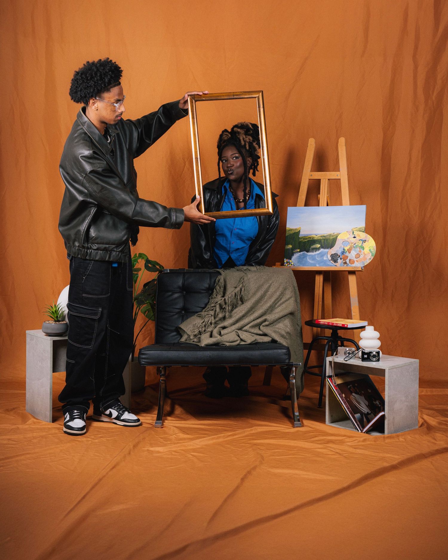 Artist wearing black creates colorful paintings on a canvas against an orange background in a sequential photo series.