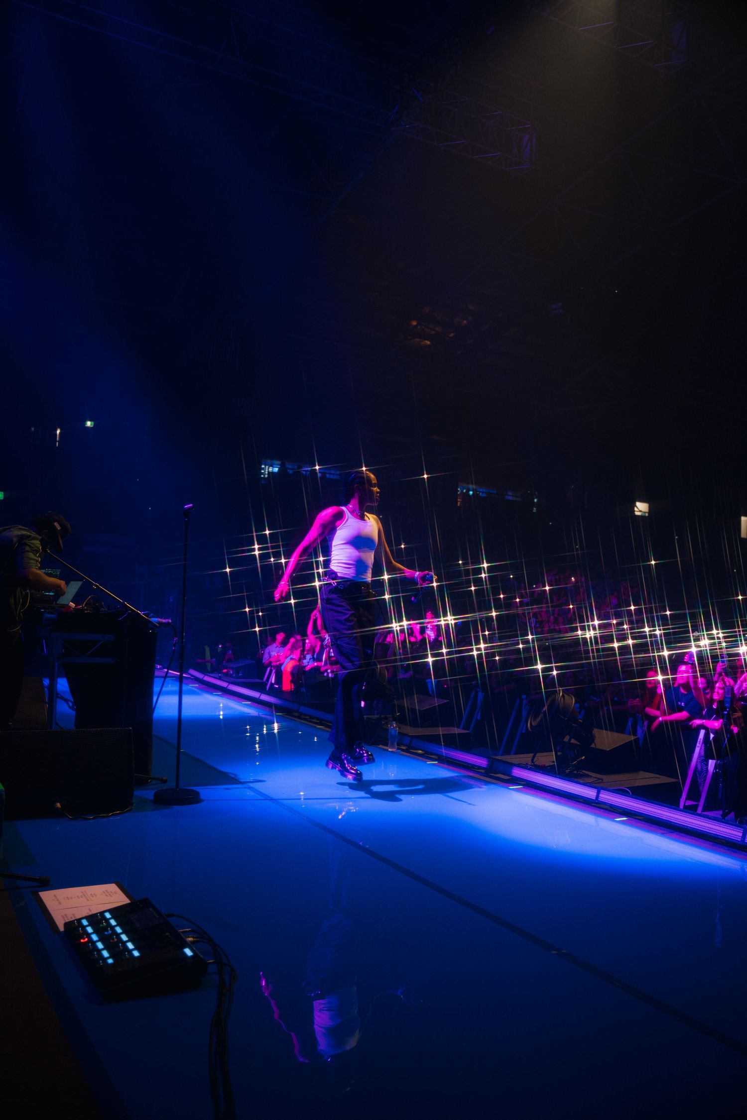 A performer jumps mid-air during a circus act under dramatic blue lighting and sparkling effects on stage.