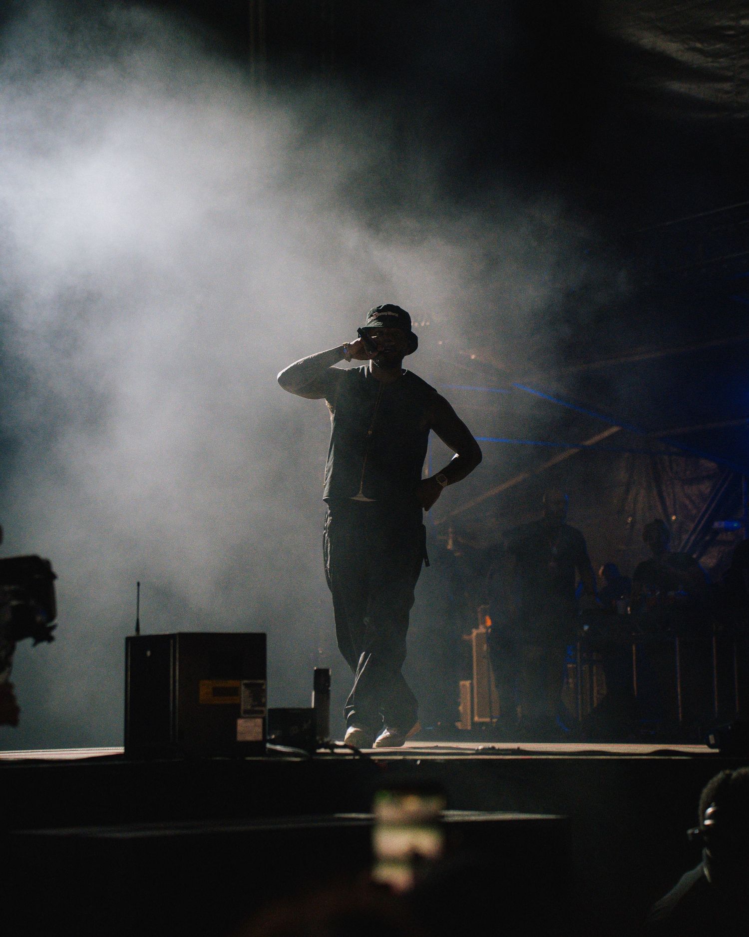 Silhouetted performer stands on stage with dramatic backlighting and fog effects during live concert performance.