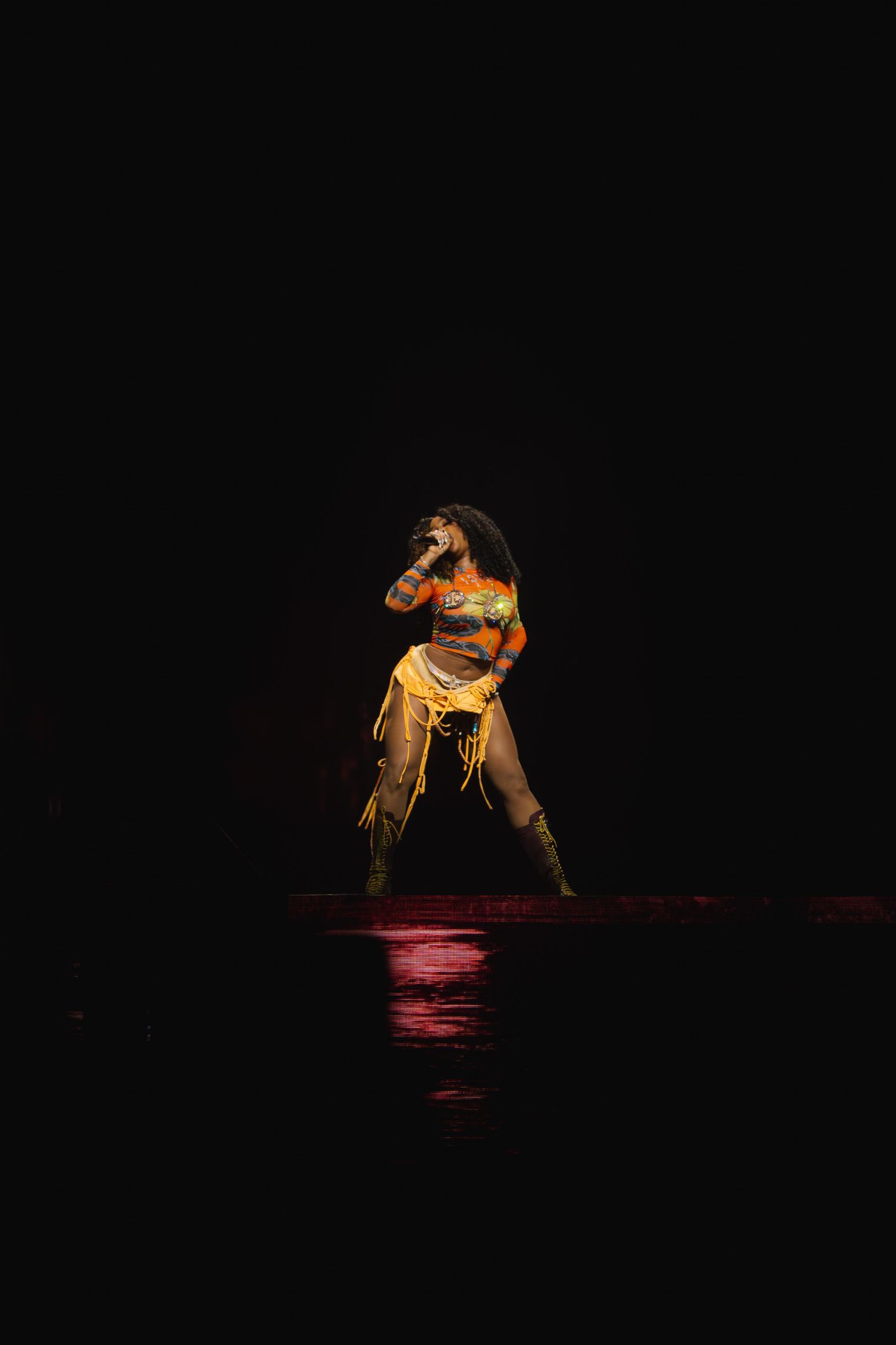Performer in yellow costume dances alone on dark stage with dramatic red lighting reflection below.